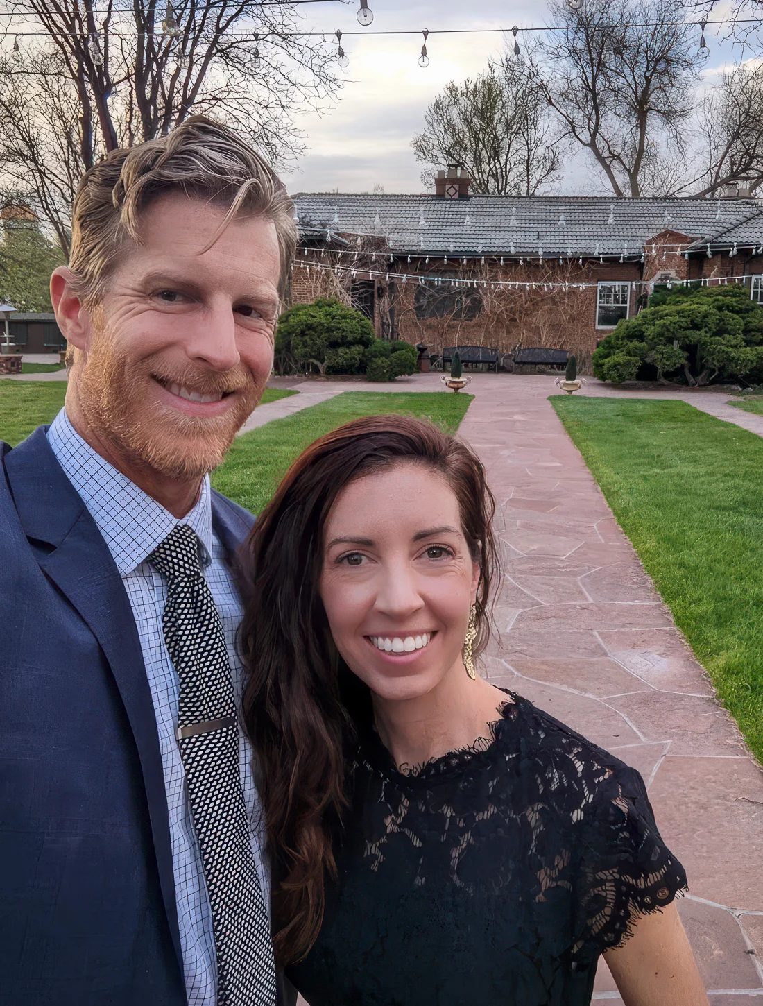 Cody and Holly Strate on a lawn under string lights, a brick house behind them.