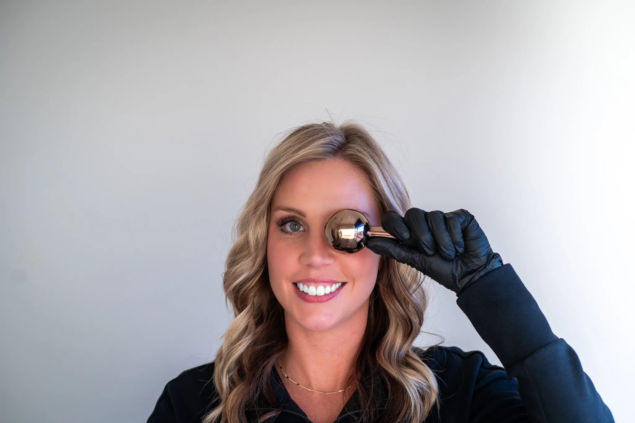 A smiling FACE Colorado team member holds a polished metal facial globe over one eye with a black-gloved hand.