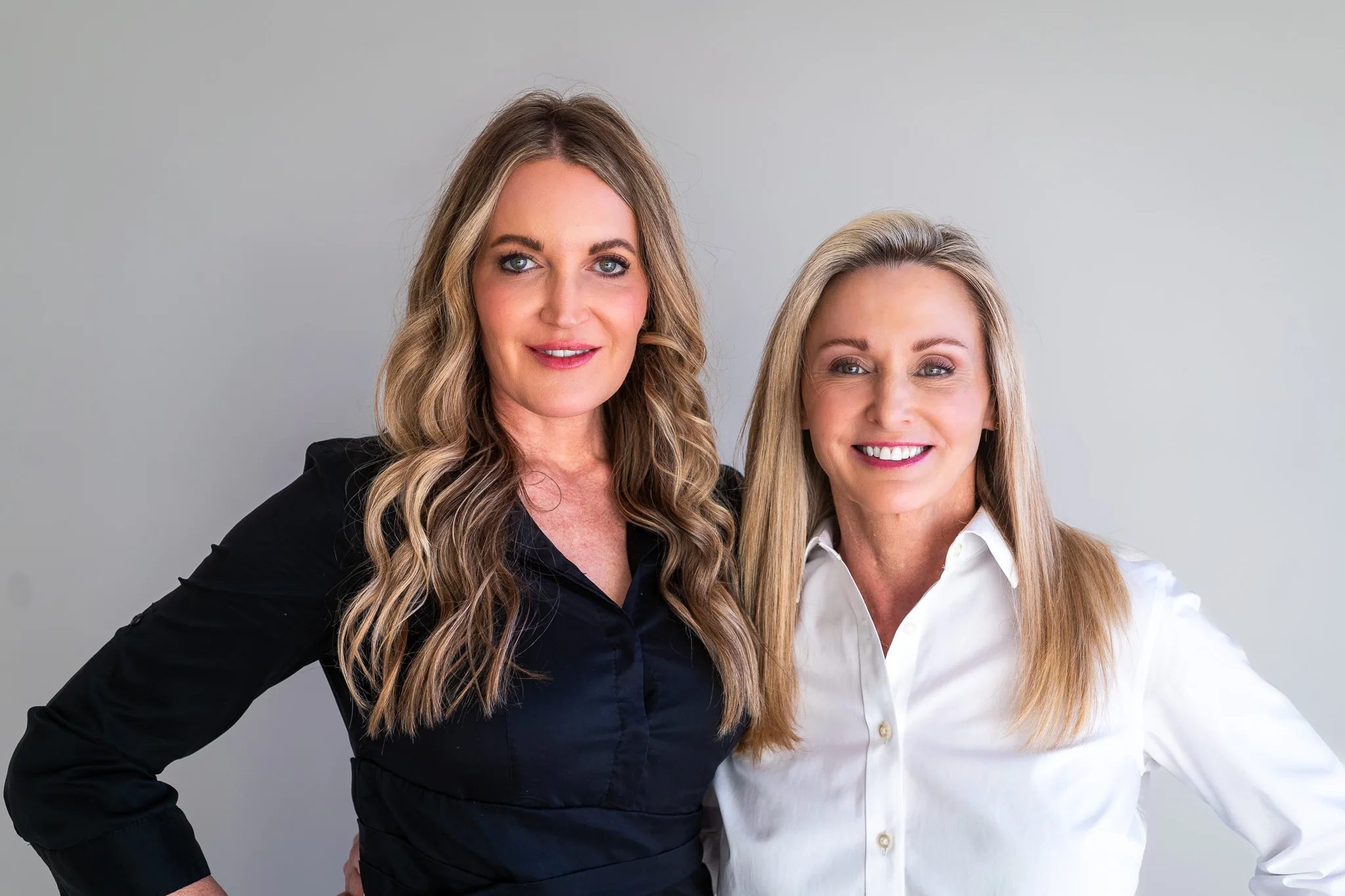 Two FACE Colorado nurses pose side by side, one in a black button-up shirt and one in a white button-up, against a grey studio backdrop.