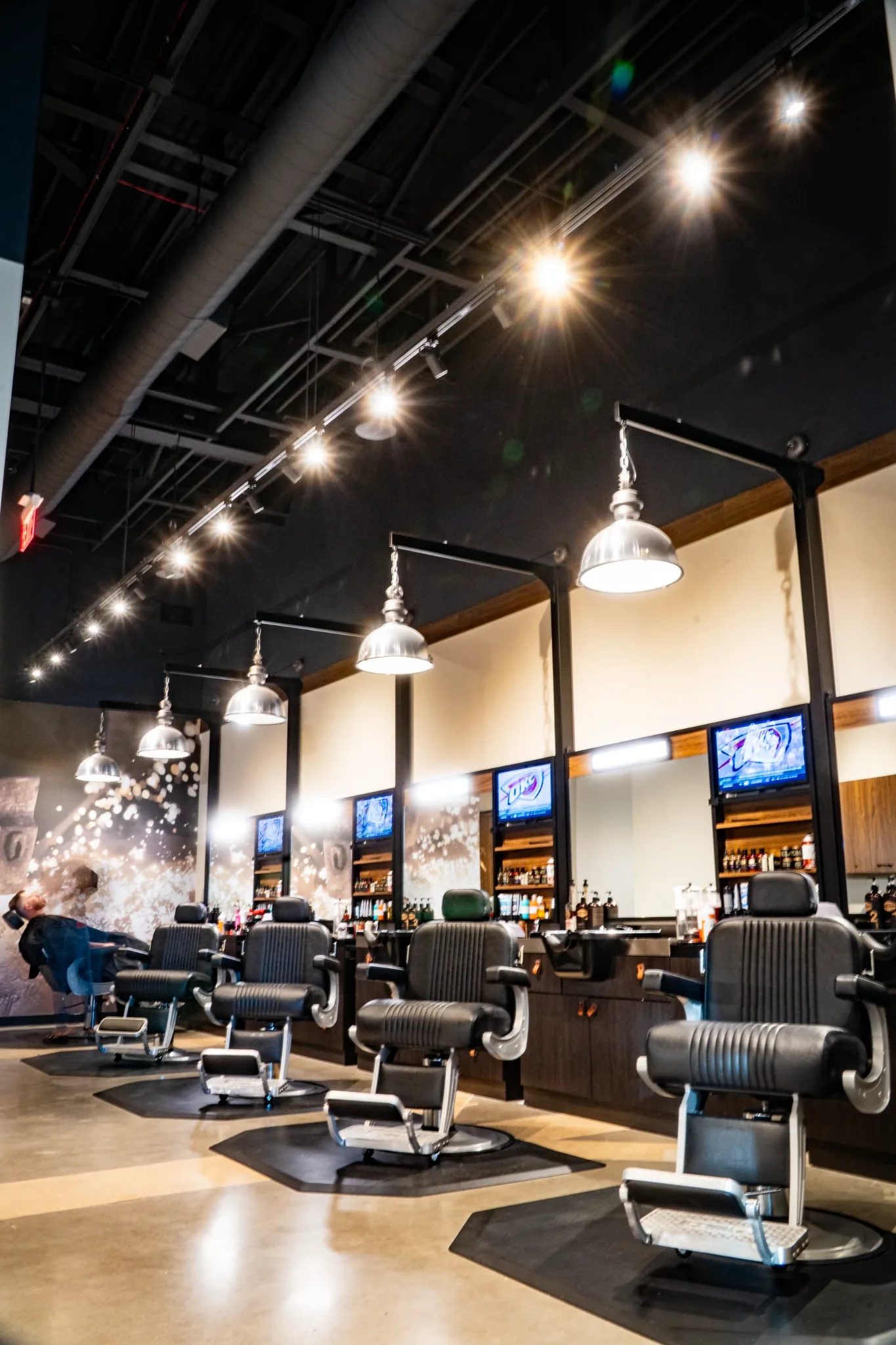 Barber chairs and chrome pendant lights under a black ceiling at Hammer & Nails in Mansfield, Texas, built by The Charles Morgan Group
