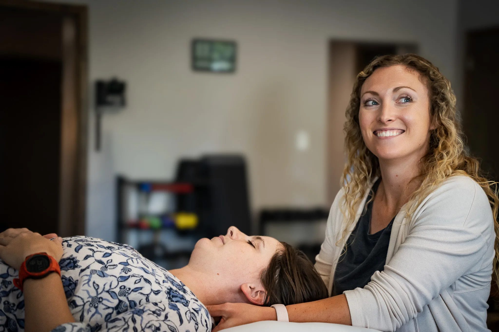 A physical therapist smiles while treating a patient's neck on a treatment table at an IRG Hand & Physical Therapy clinic.