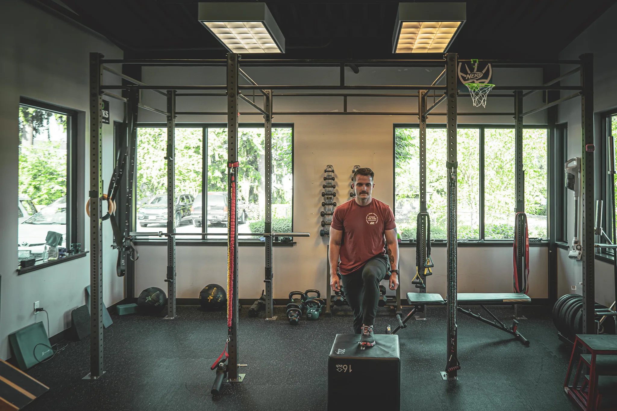 A person steps up onto a plyo box beneath a steel training rig in an IRG Hand & Physical Therapy clinic gym.