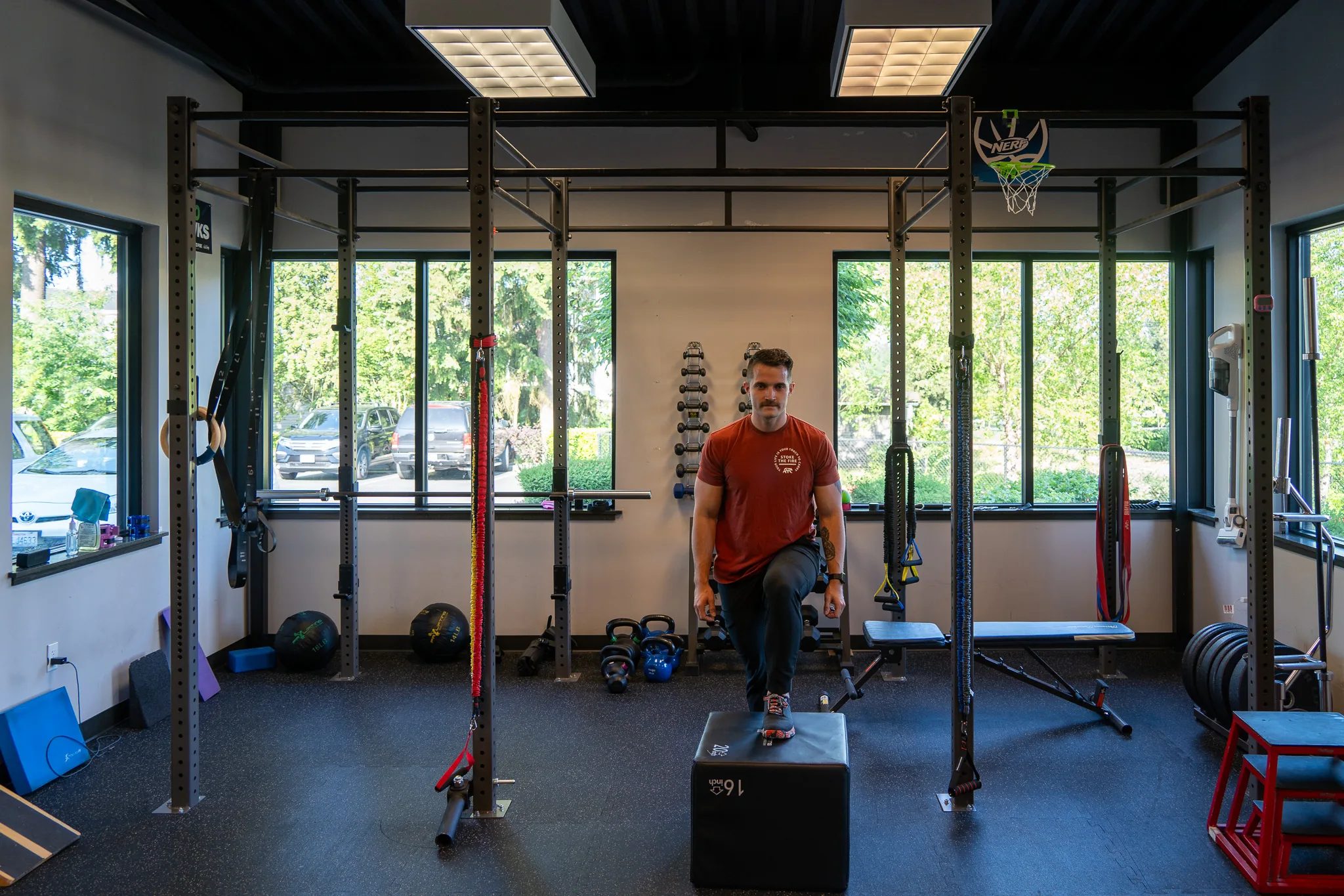 A person balances one foot on a plyo box under a steel training rig in a bright IRG Hand & Physical Therapy gym.