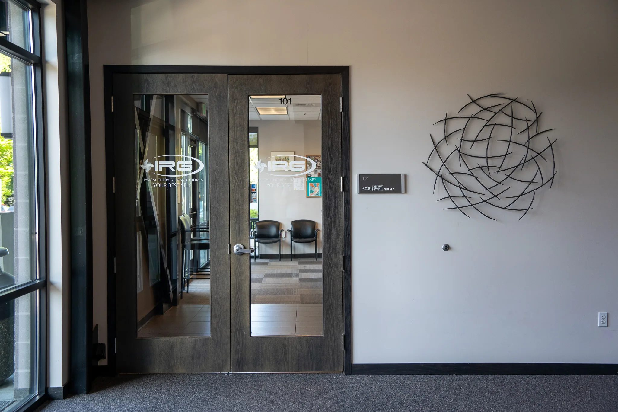 Double wood-and-glass doors to IRG Gateway Physical Therapy, suite 101, with the IRG logo etched on the glass and a metal sculpture on the wall.