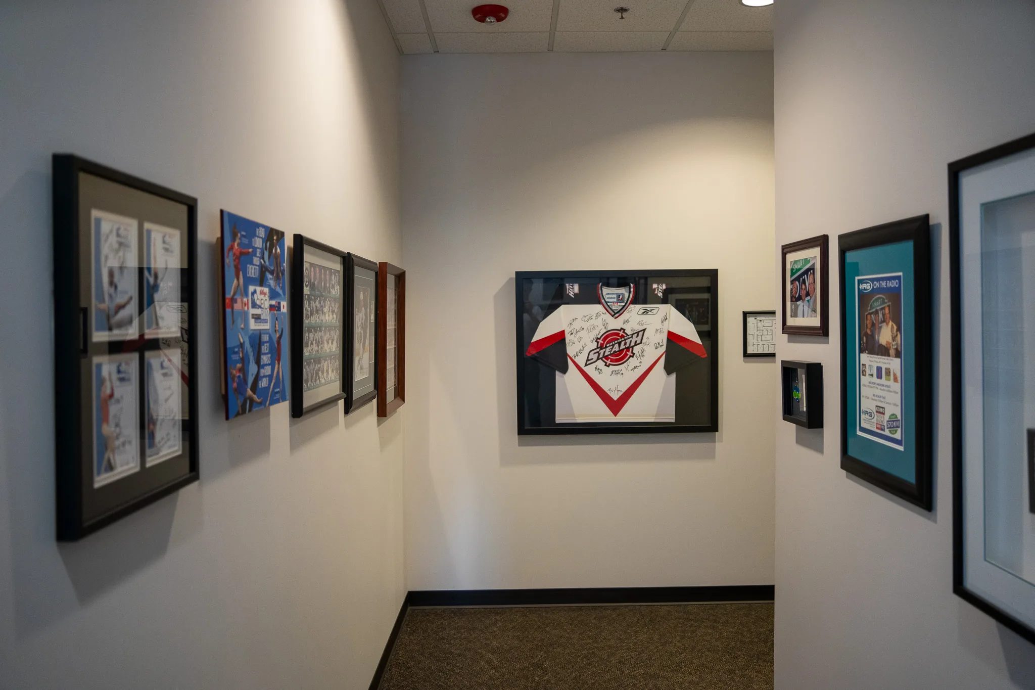 A clinic hallway at IRG Physical & Hand Therapy lined with framed sports memorabilia, including a signed Washington Stealth jersey.