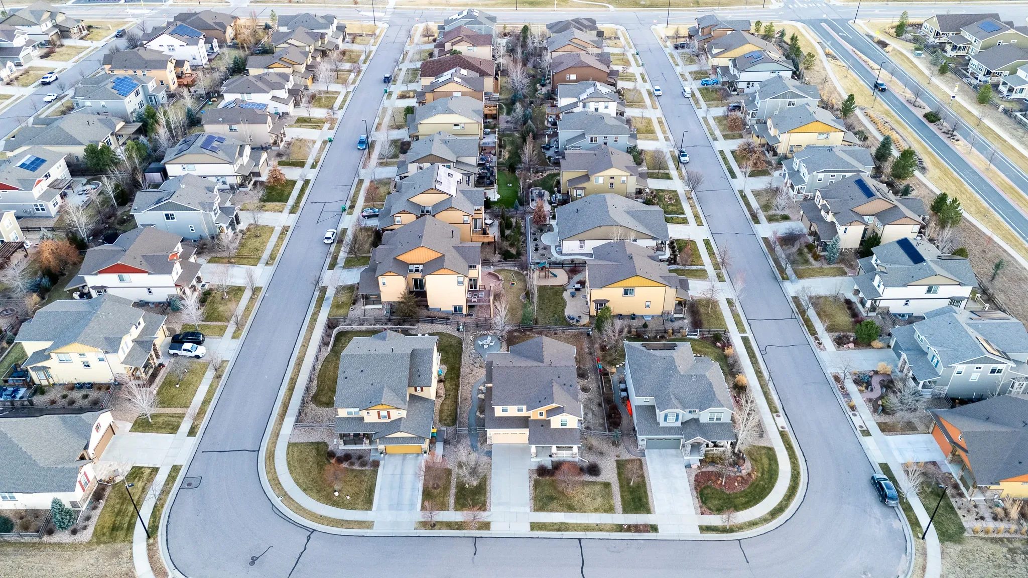 High-angle drone view of two rows of two-story homes with rooftop solar panels in a Denver-area subdivision.