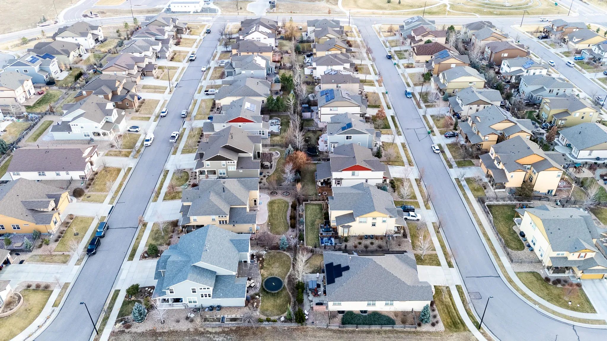 Drone view of suburban homes backing onto a shared greenway of bare trees in a Denver-area subdivision.