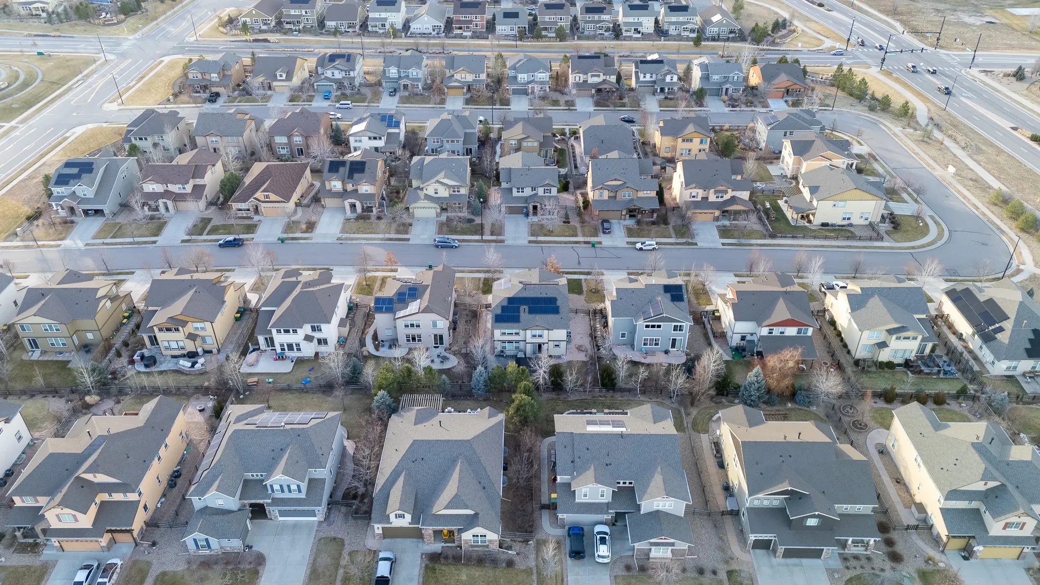 Drone view over dense rows of two-story homes and a signalized intersection in a Denver-area subdivision.
