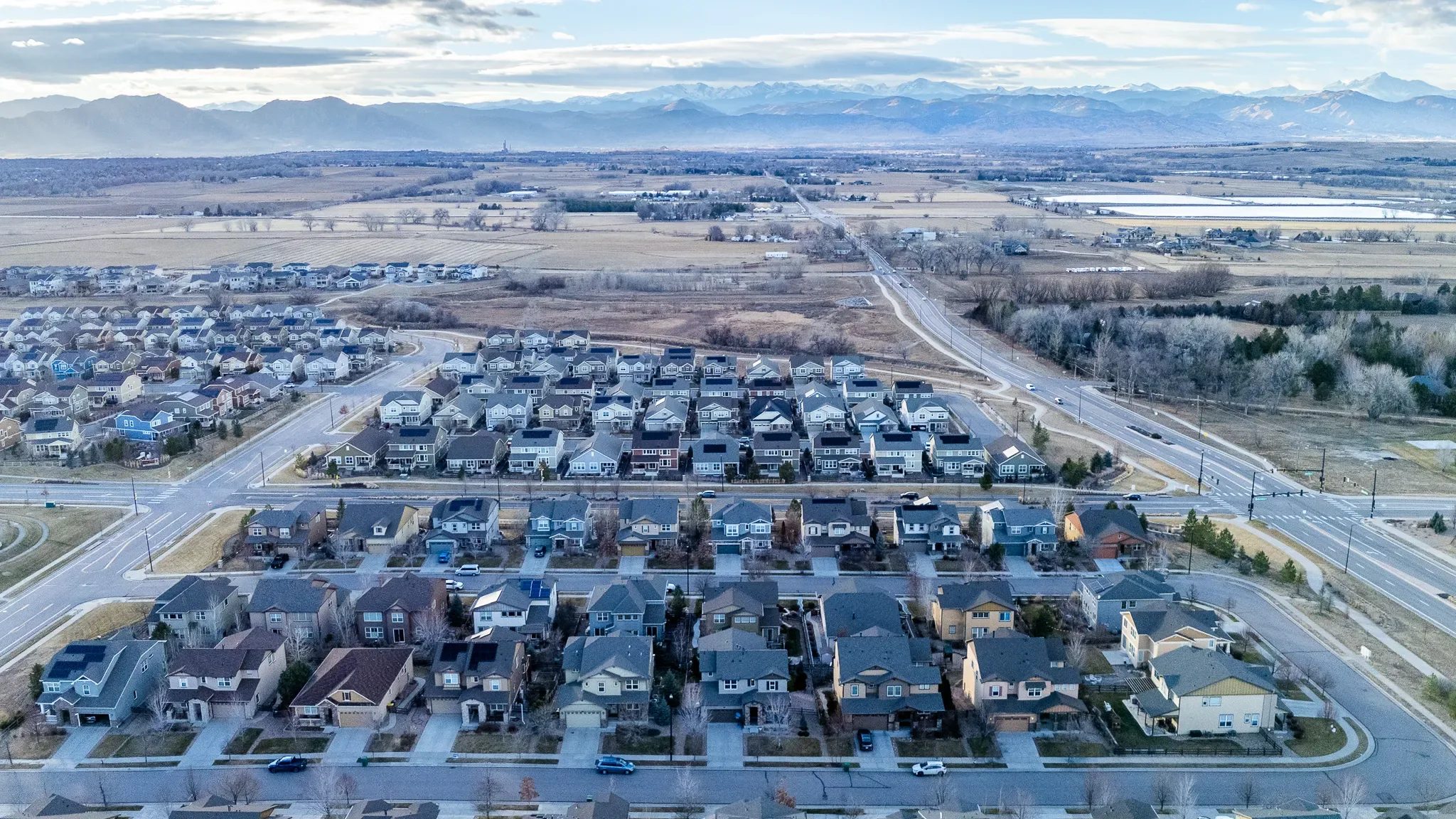 Aerial view of a Denver-area subdivision with rows of new homes, open fields and the Front Range mountains on the horizon.