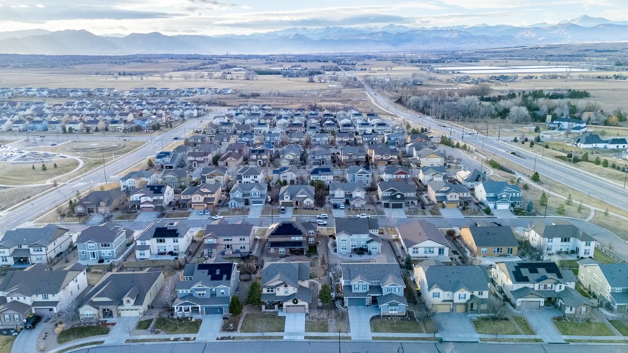 Drone view of a Denver-area neighborhood with a community park, rows of homes and snow-dusted mountains in the distance.