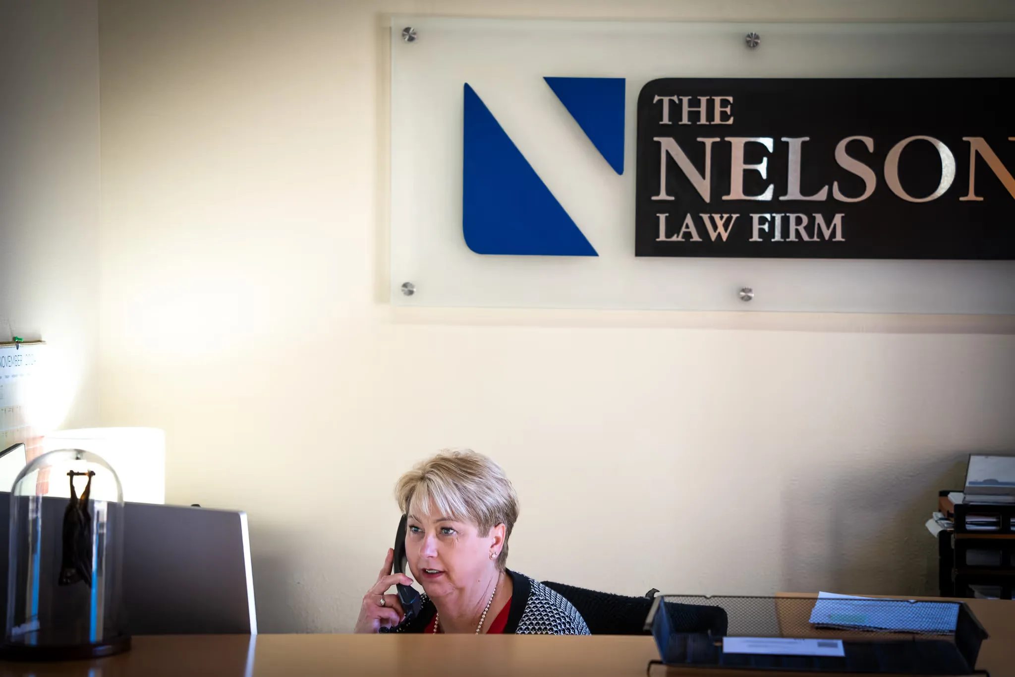 A staff member answers the phone at the Nelson Law Firm reception desk beneath the firm's wall sign.