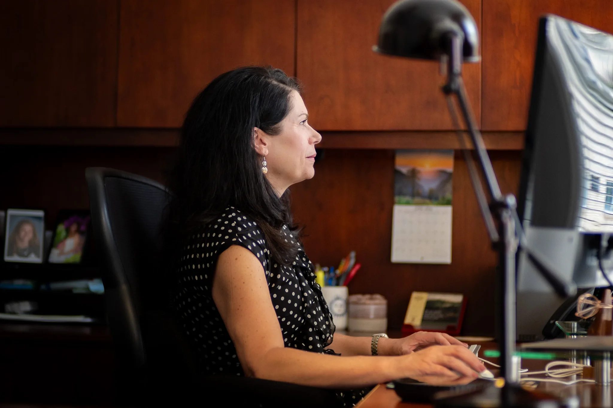 Melissa J. Hessler, Partner, types at a keyboard beneath a desk lamp in a wood-paneled office at Nelson Law Firm.