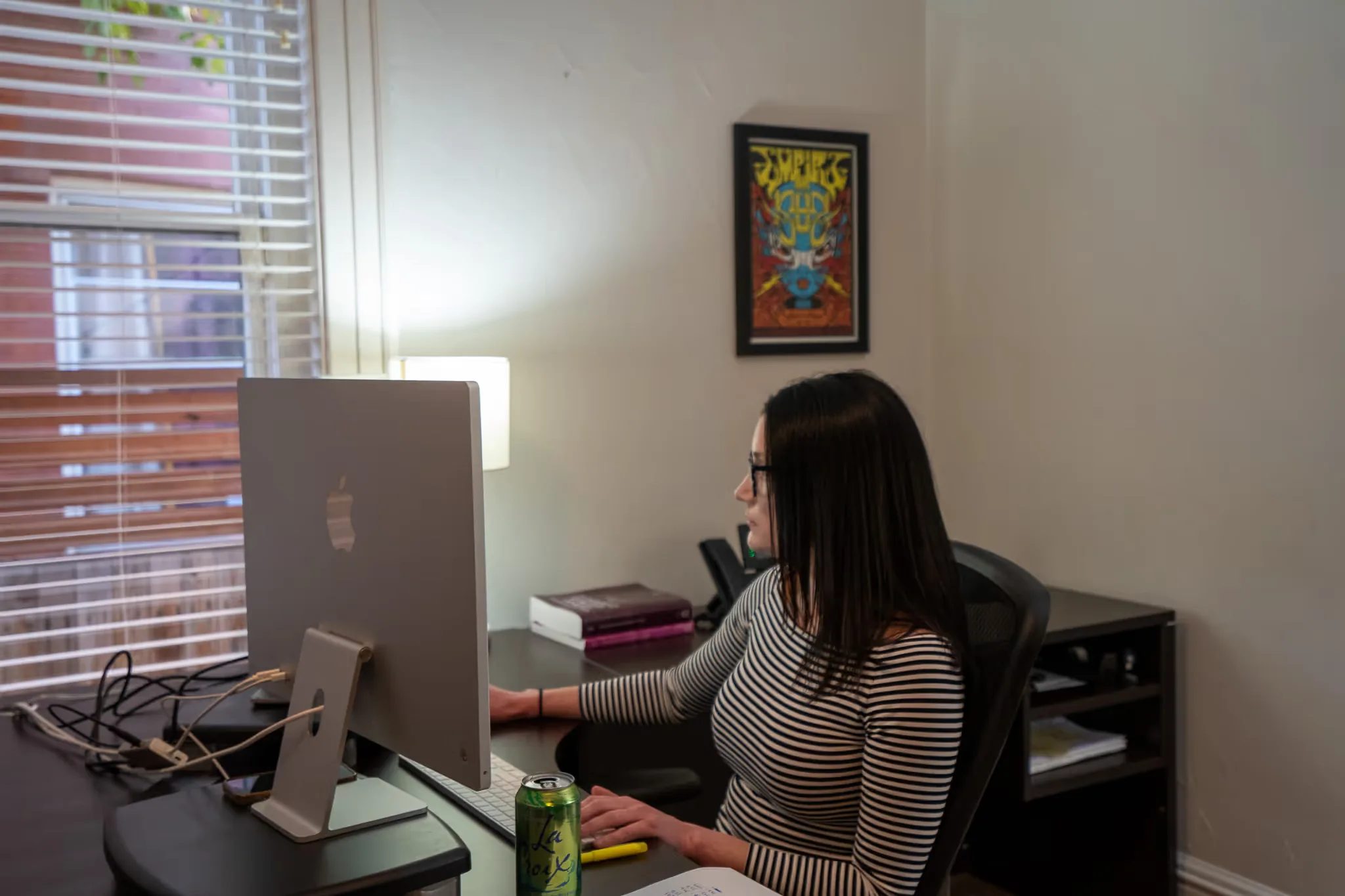 A staff member works at an iMac in a bright office with a framed concert poster on the wall at Nelson Law Firm.