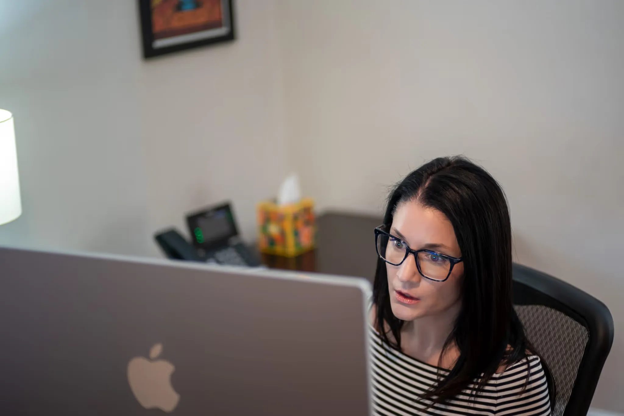 A staff member with glasses looks over the top of an iMac while working at Nelson Law Firm.