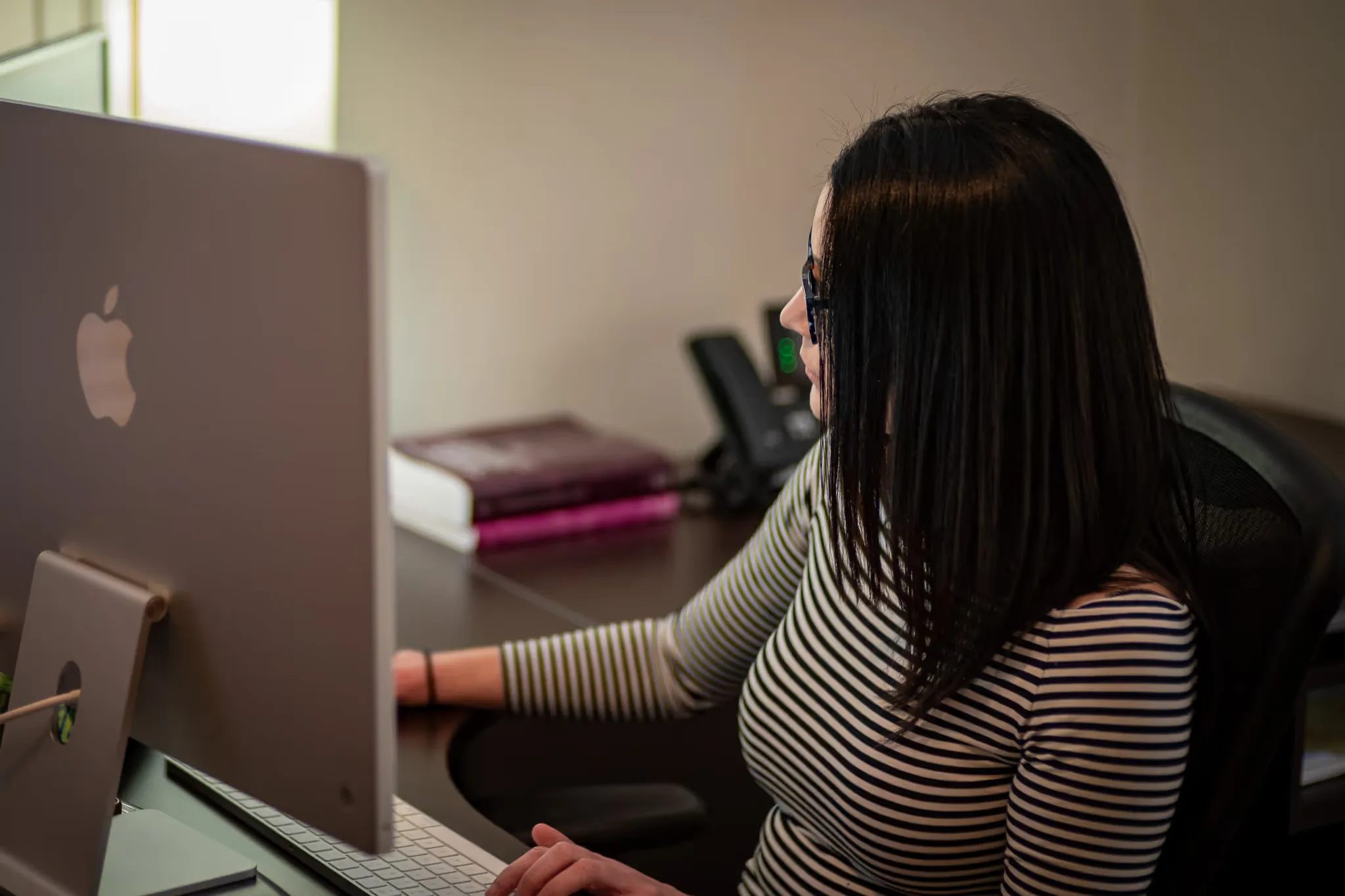 Side view of a staff member typing at an iMac keyboard in a Nelson Law Firm office.