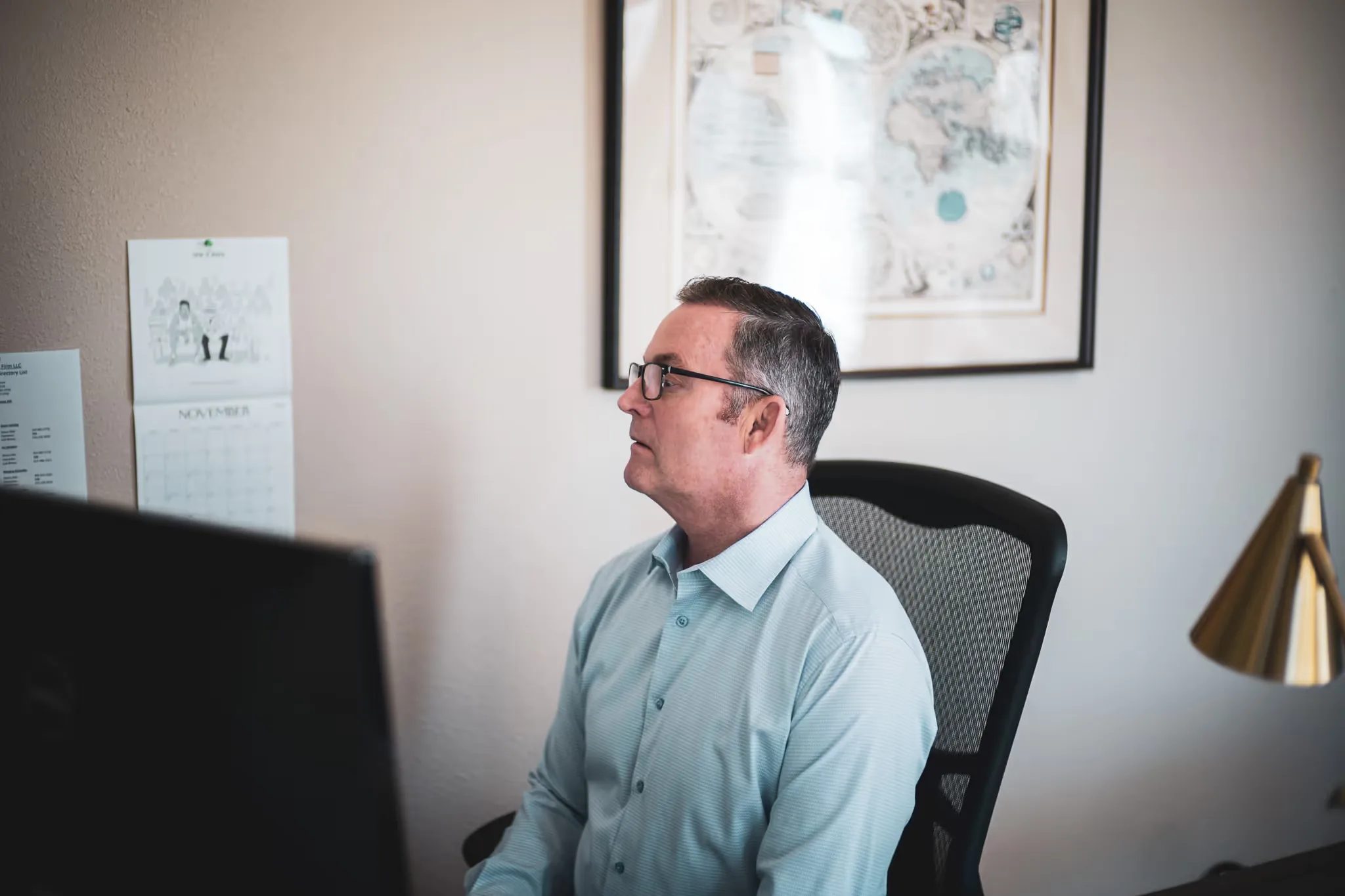 A staff member with glasses studies a monitor at a desk beneath a framed antique world map at Nelson Law Firm.