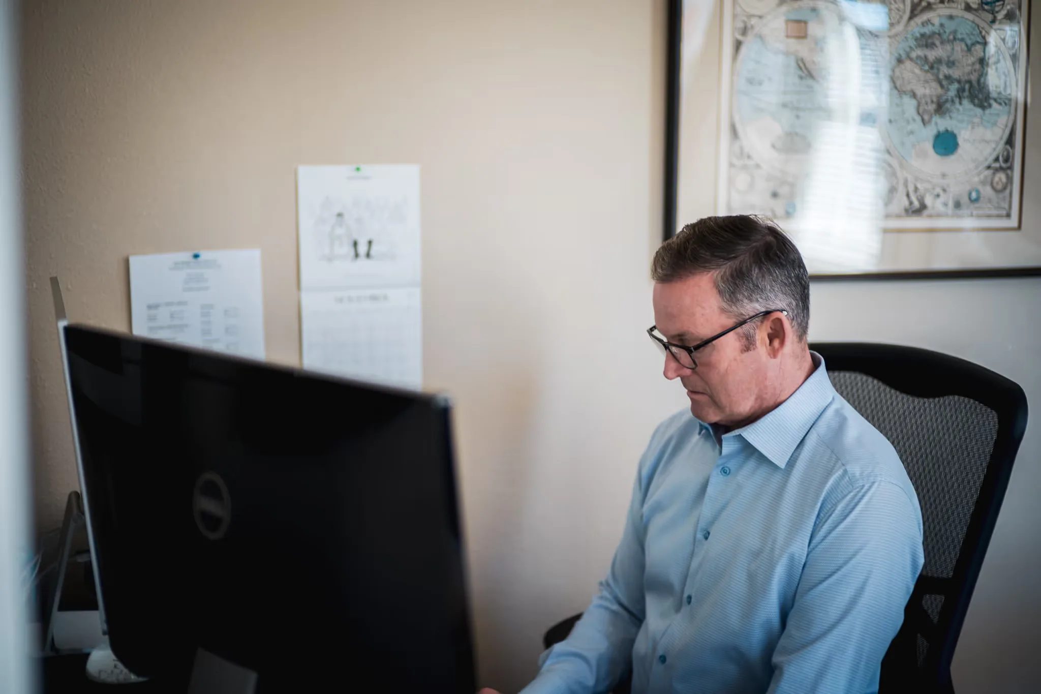 A staff member looks down at a monitor at a desk with an antique world map on the wall at Nelson Law Firm.