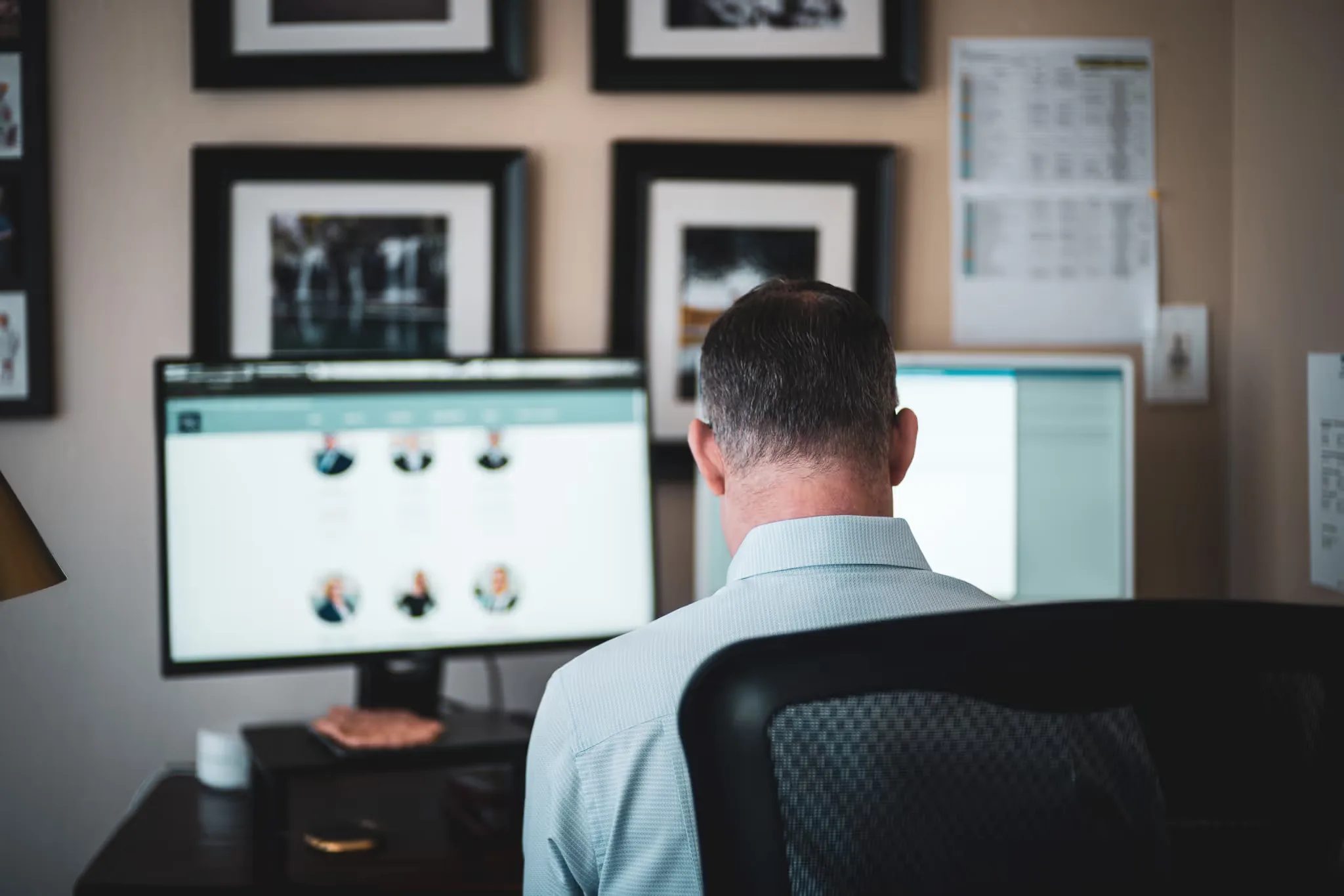 Seen from behind, a staff member reviews a team-directory webpage on dual monitors at Nelson Law Firm.