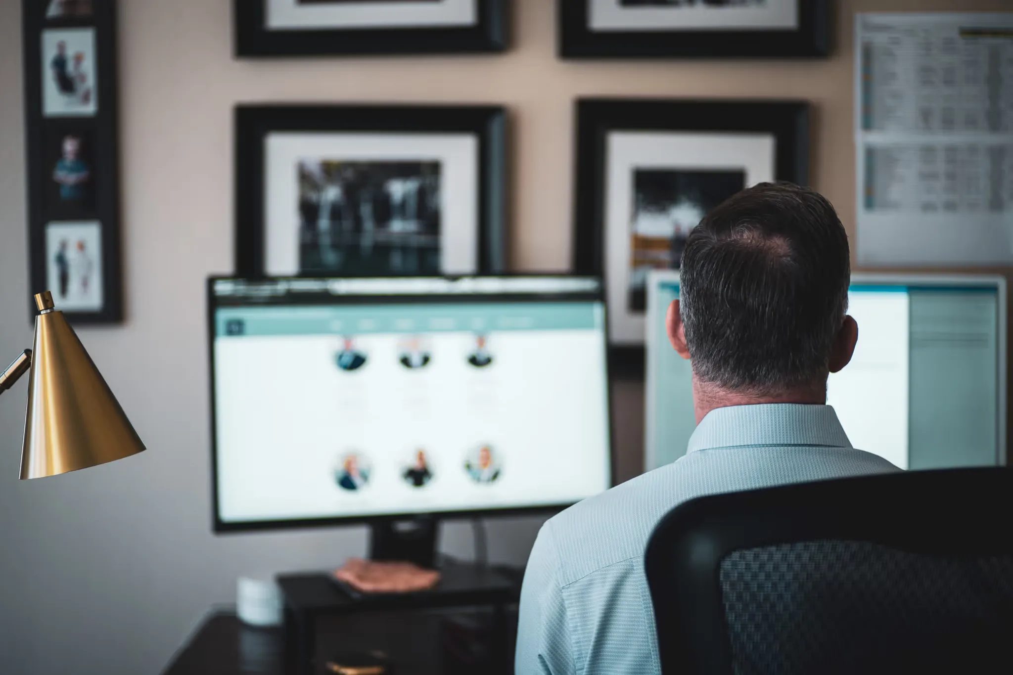 Over-the-shoulder view of a staff member at dual monitors beside a brass lamp, framed photos on the wall at Nelson Law Firm.