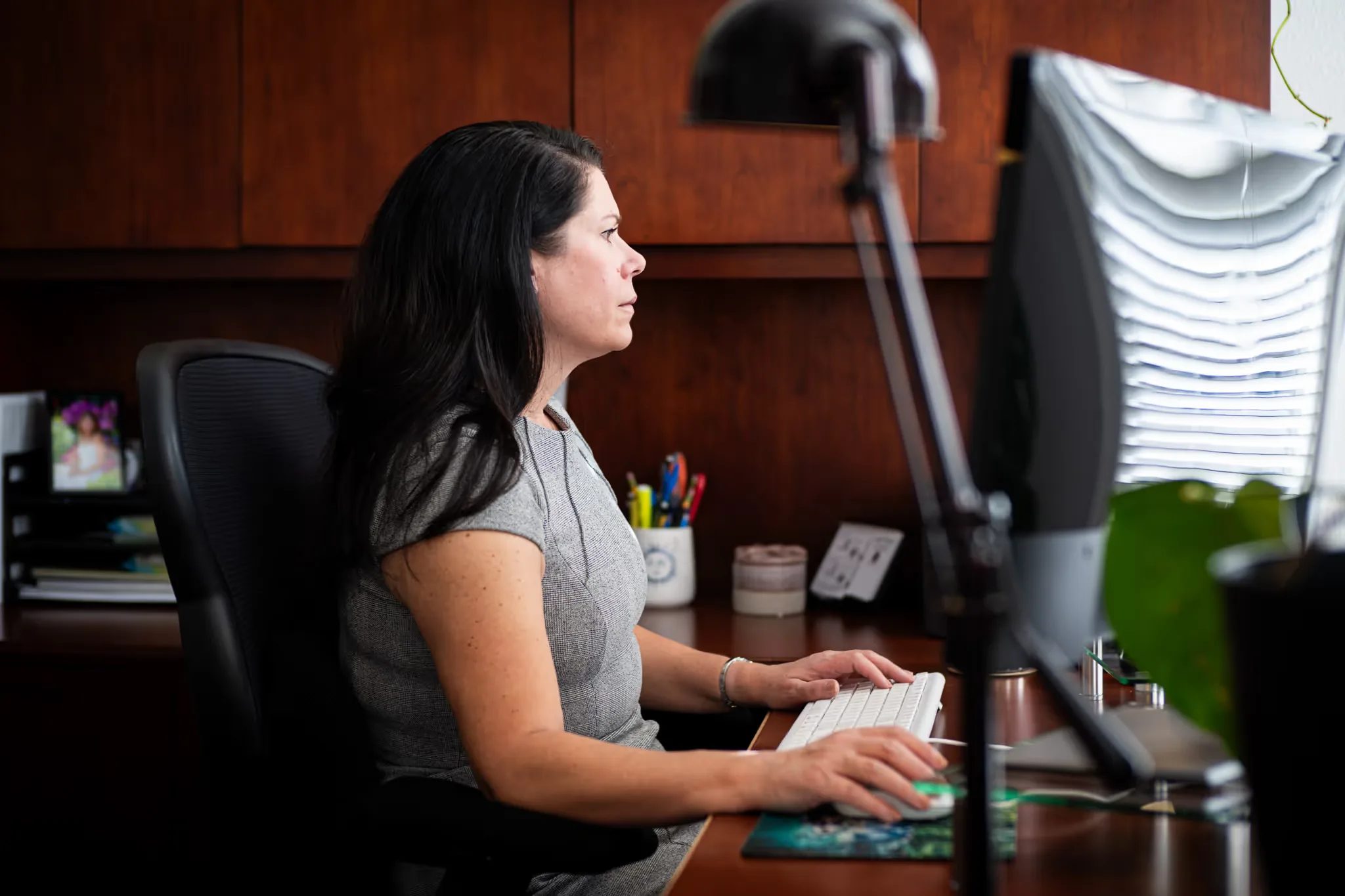 A staff member in a grey dress works at a computer in a wood-paneled office at Nelson Law Firm.