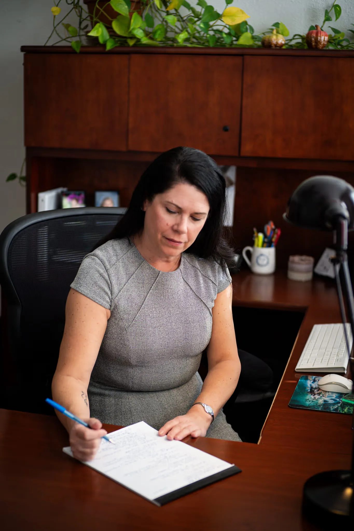 A staff member writes notes on a document at a wood desk beneath a shelf of trailing plants at Nelson Law Firm.