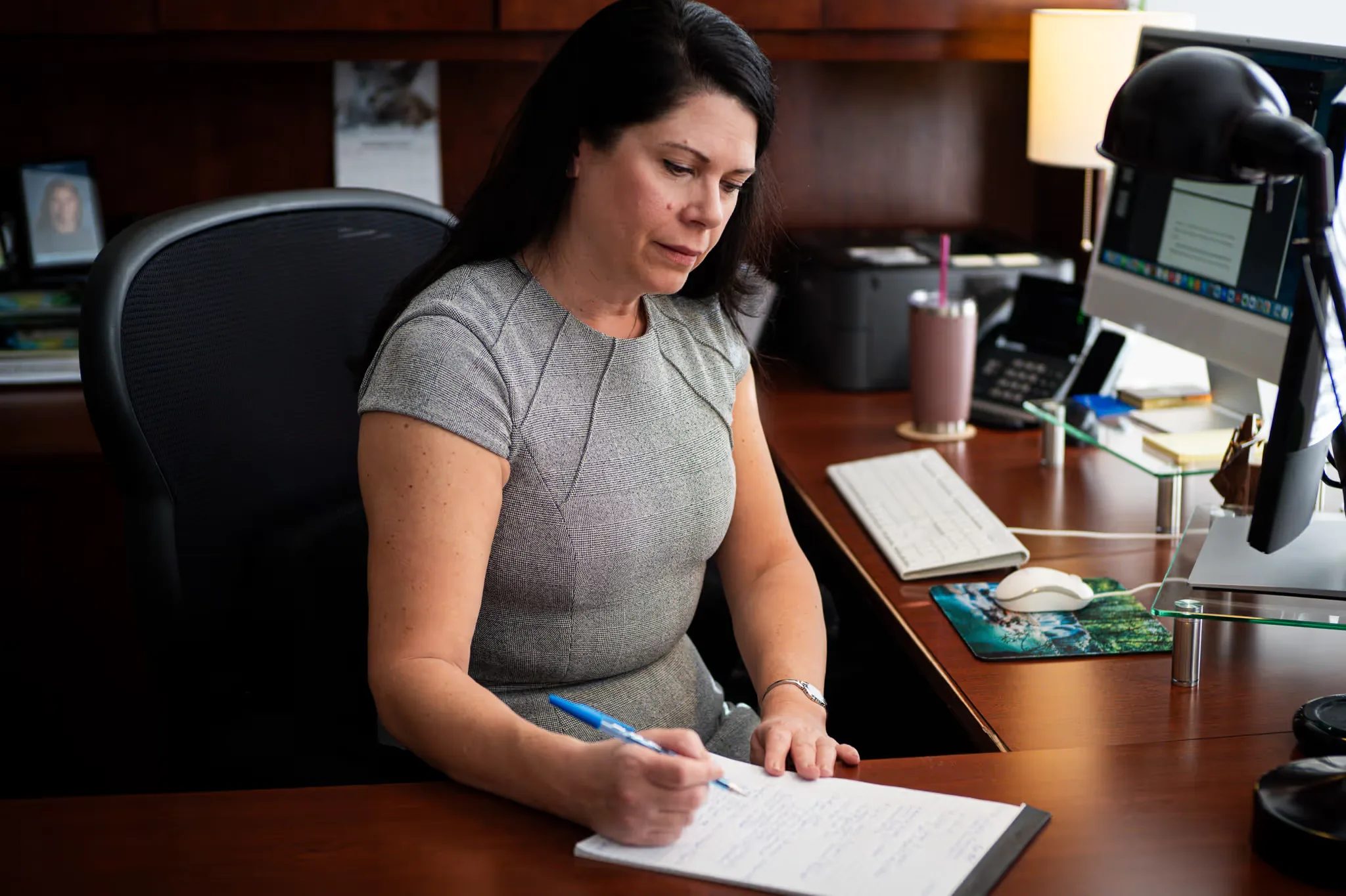 A staff member annotates a handwritten document at a desk with a monitor and desk phone at Nelson Law Firm.