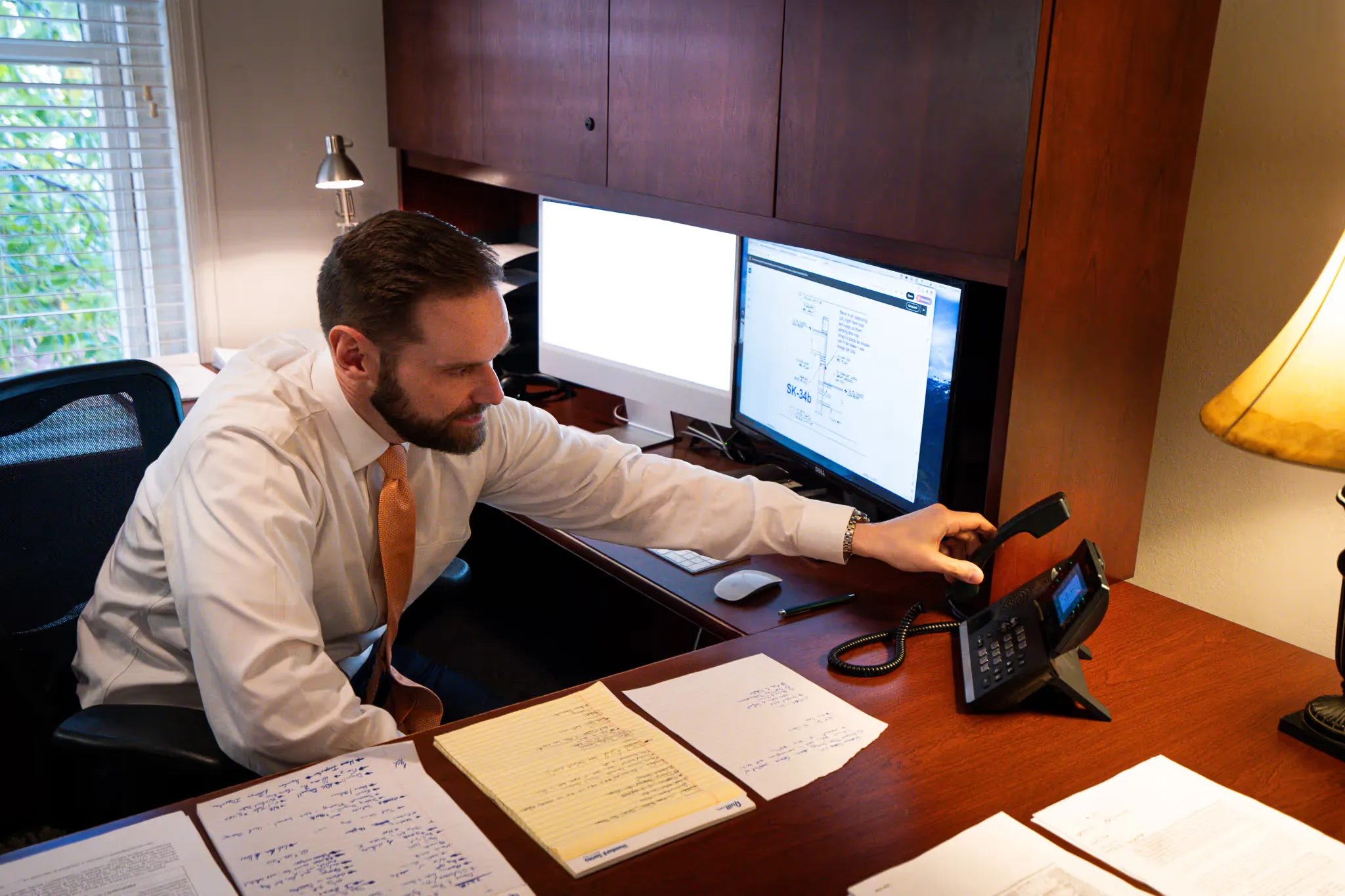 A staff member reaches for a desk phone handset beside a monitor showing a technical drawing at Nelson Law Firm.