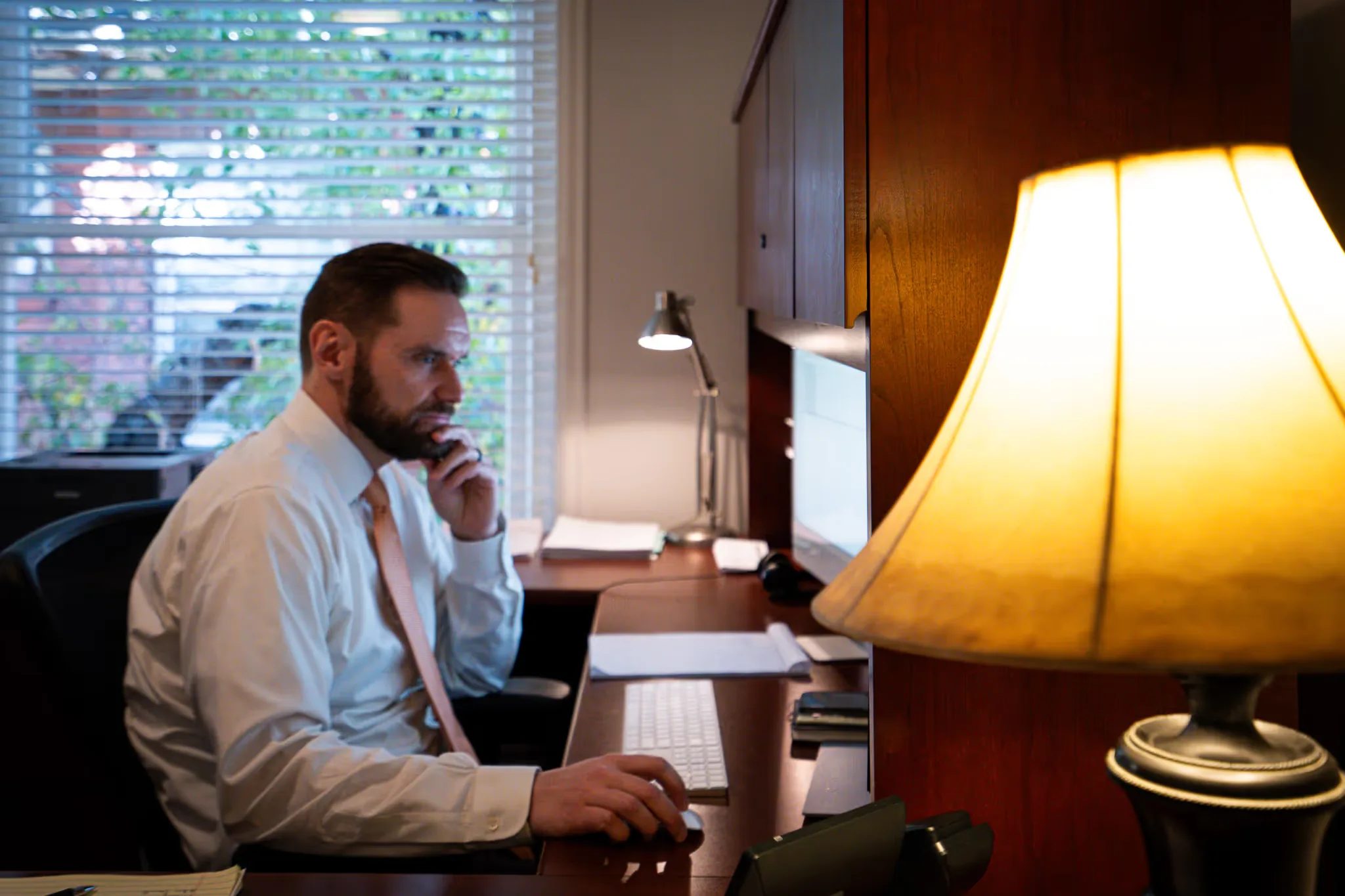 A staff member, chin in hand, studies a monitor beside a glowing table lamp at Nelson Law Firm.