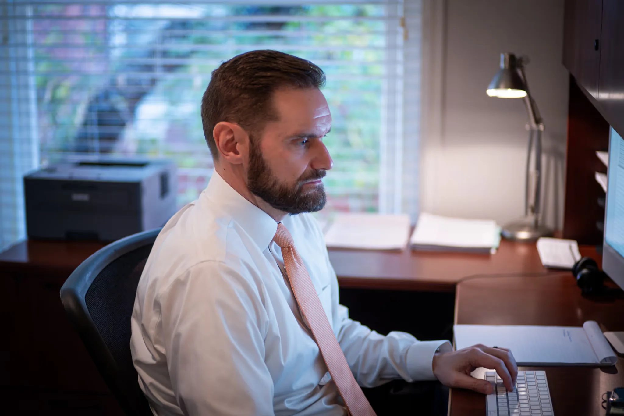 Profile of a staff member in a white shirt and orange tie typing at a keyboard by a window at Nelson Law Firm.