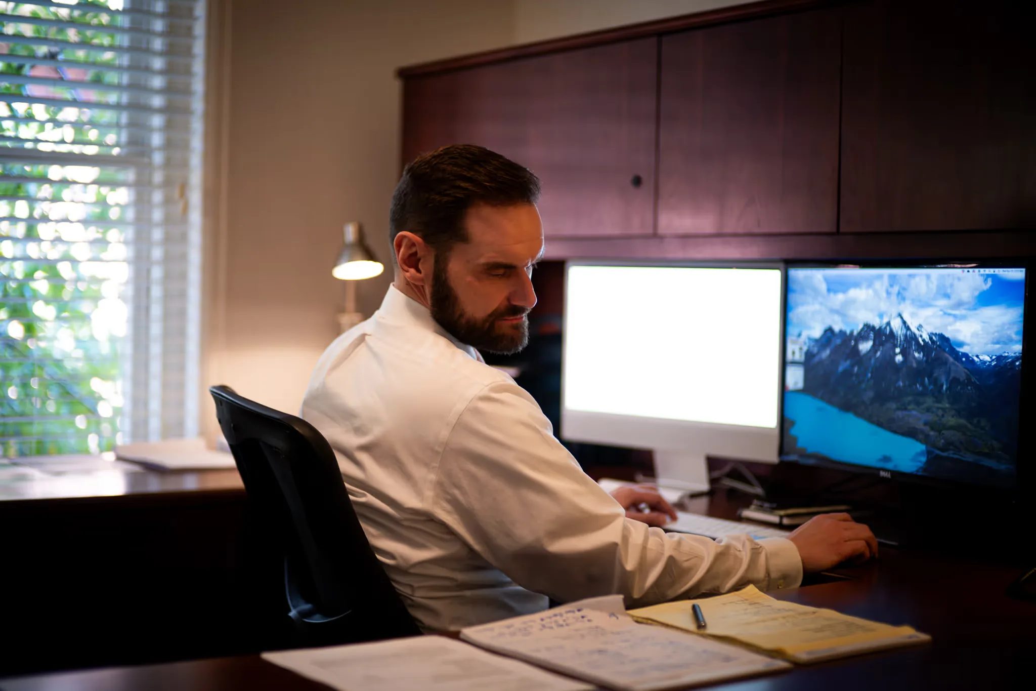 A staff member turns toward a legal pad at a desk with dual monitors and a wood hutch at Nelson Law Firm.