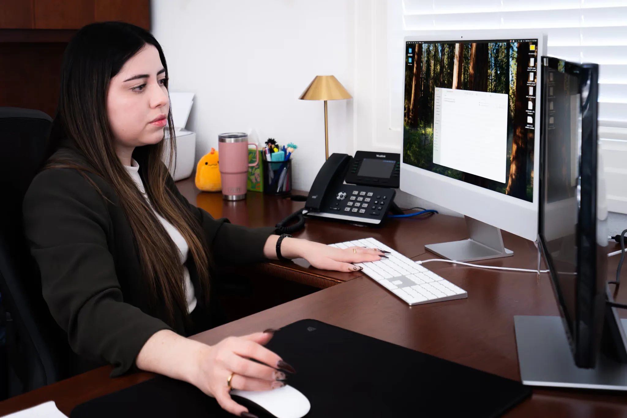 Mariana Gonzalez, Paralegal, works at an iMac with a desk phone and a brass lamp in a Nelson Law Firm office.