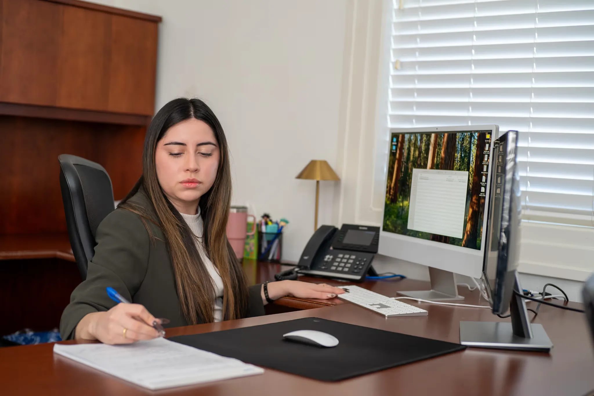 Mariana Gonzalez, paralegal, writing notes at a desk with two monitors in the Nelson Law Firm office in Denver