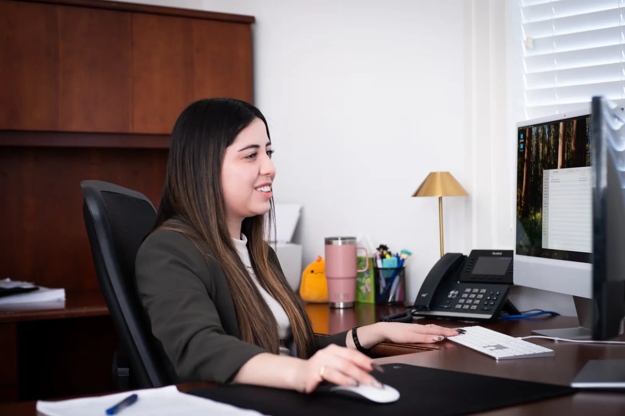 Mariana Gonzalez, paralegal, smiling at a computer monitor while working at a desk in the Nelson Law Firm office