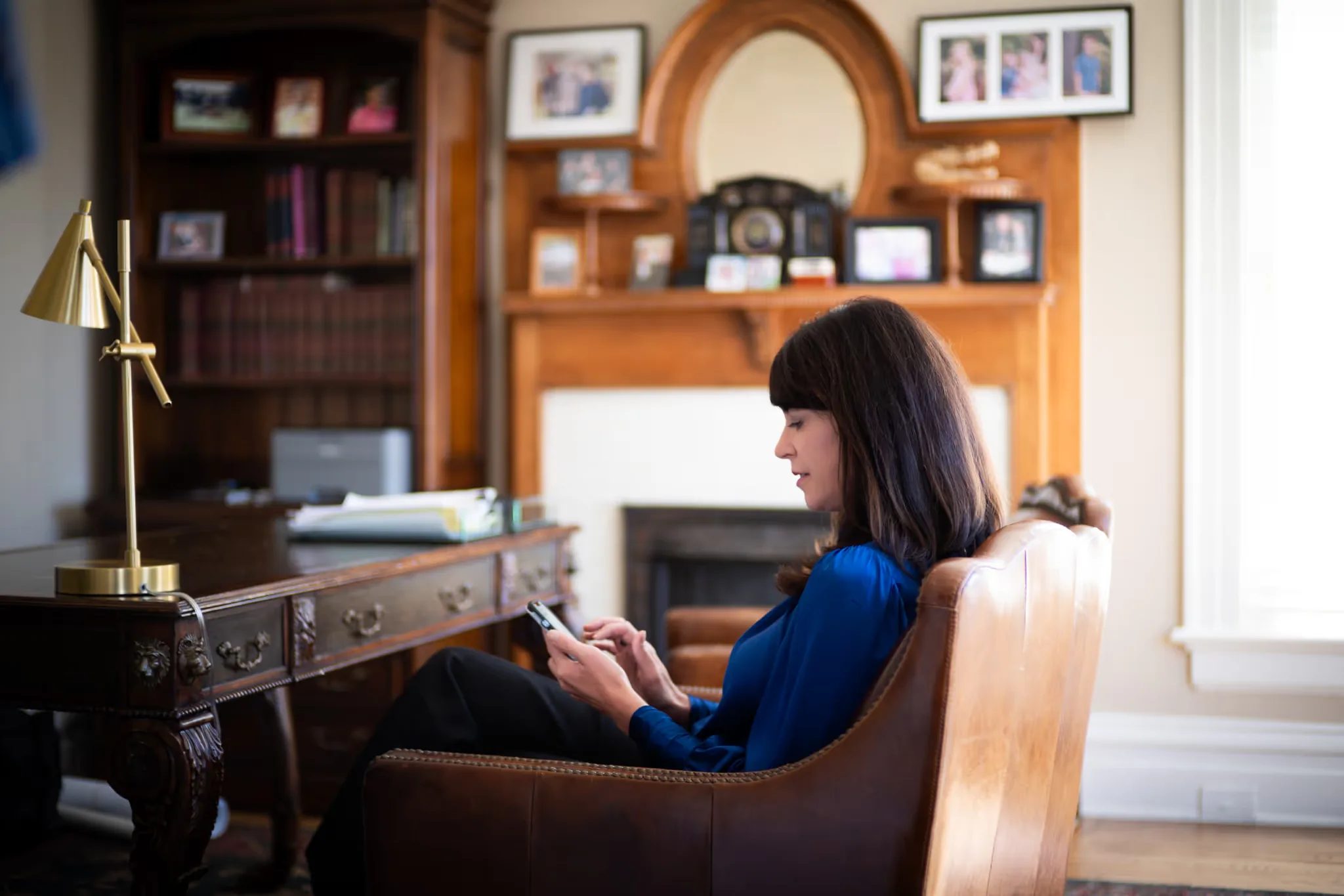Colleen S. Nelson, co-founder of Nelson Law Firm, reading on a phone in a leather armchair beside a carved fireplace mantel