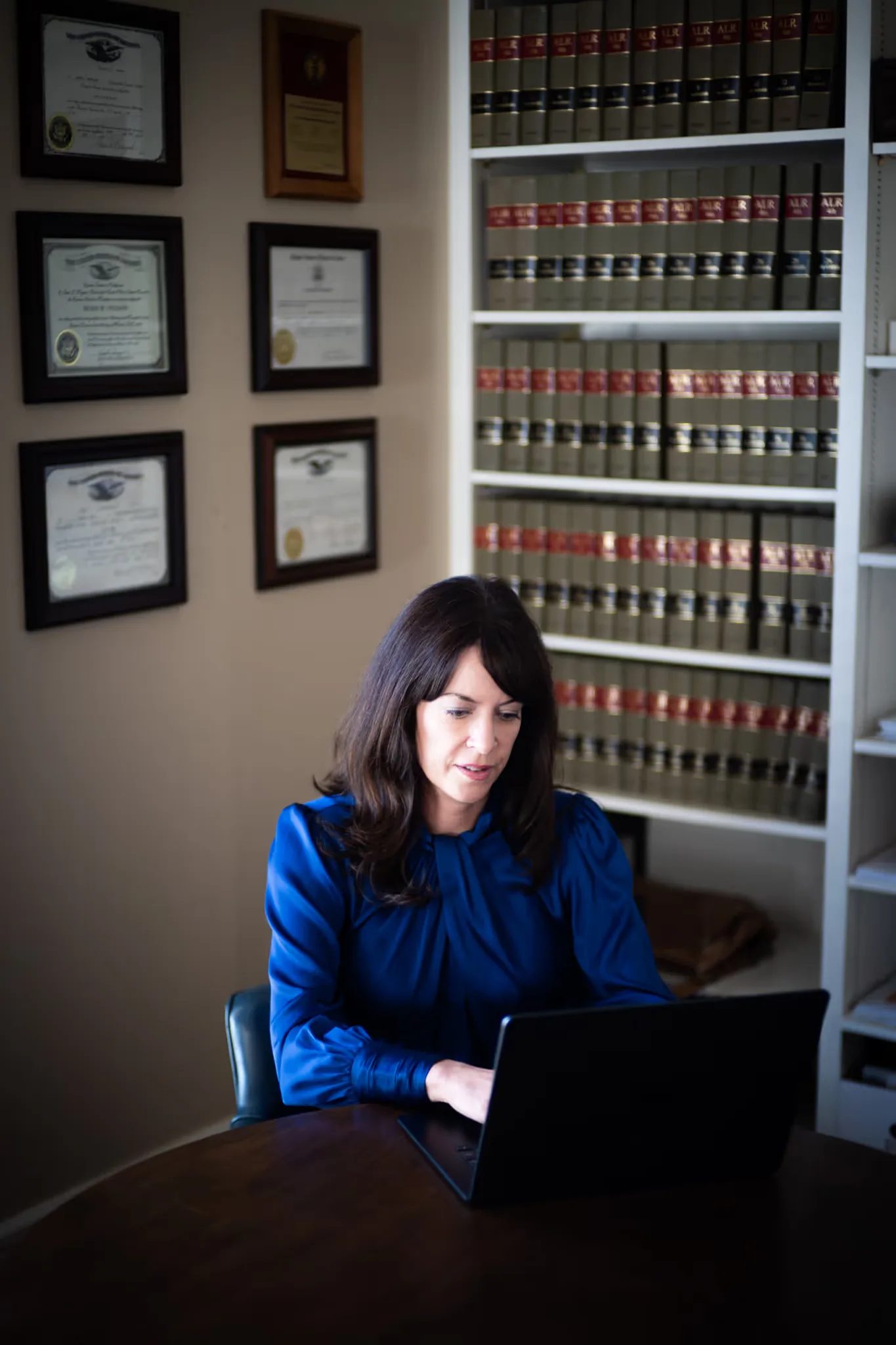 Colleen S. Nelson working on a laptop in front of shelves of law reporters and framed certificates at Nelson Law Firm