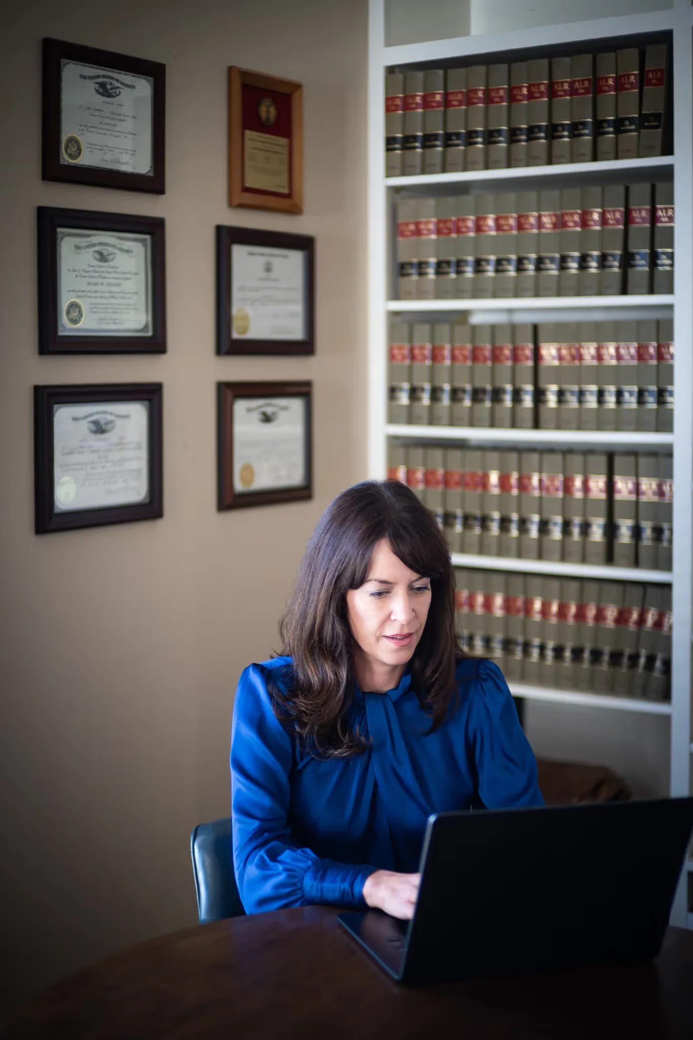 Colleen S. Nelson looking down at a laptop in front of framed diplomas and law reporters at Nelson Law Firm in Denver