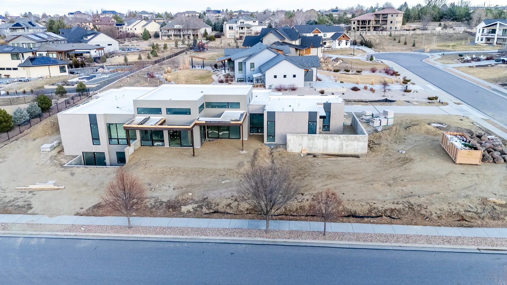 Aerial view of a modern flat-roofed home under construction on a dirt lot in a Denver-area neighborhood.
