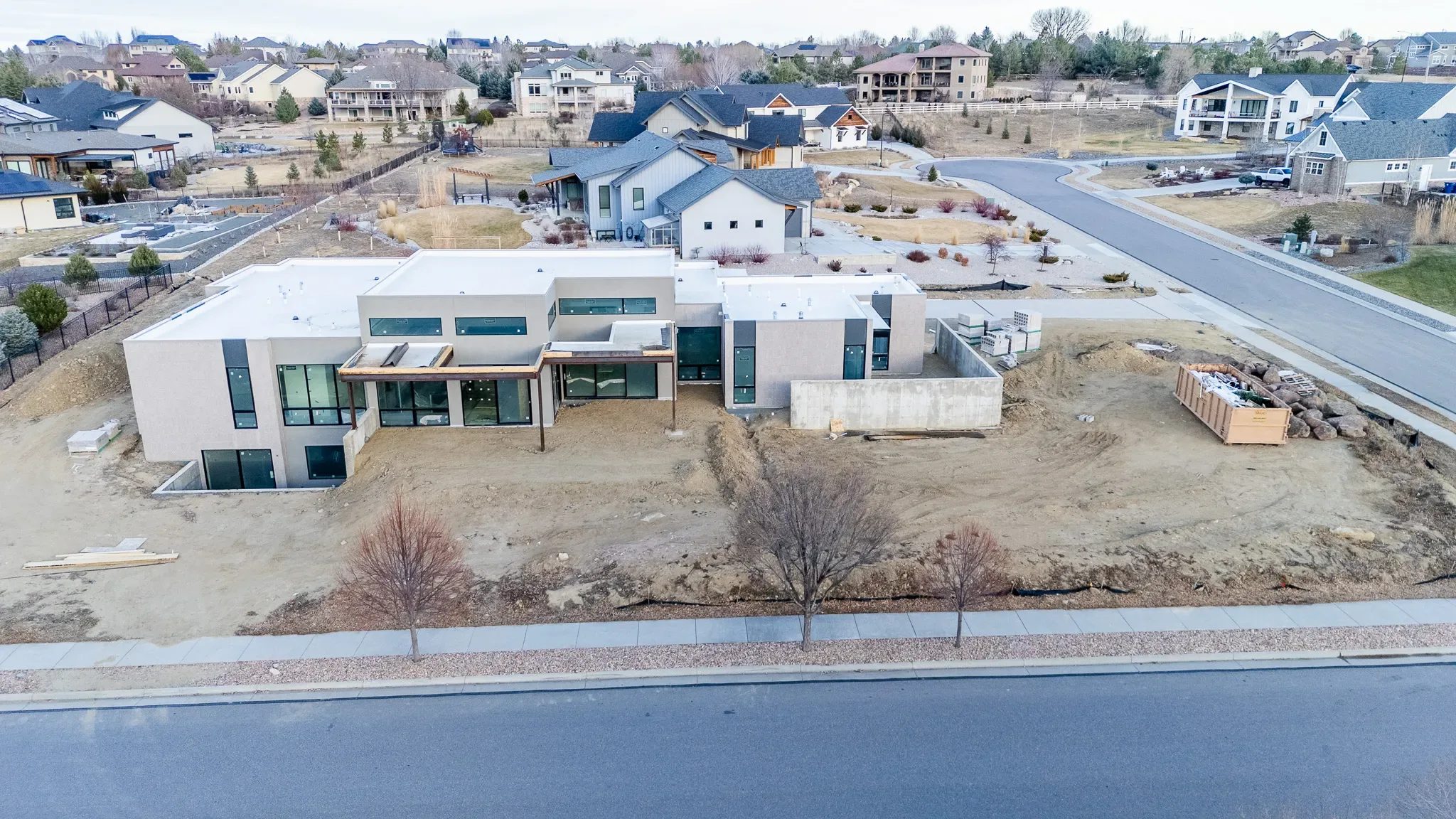 Drone view of a contemporary home under construction with white flat roofs and stacked block on a bare Denver-area lot.