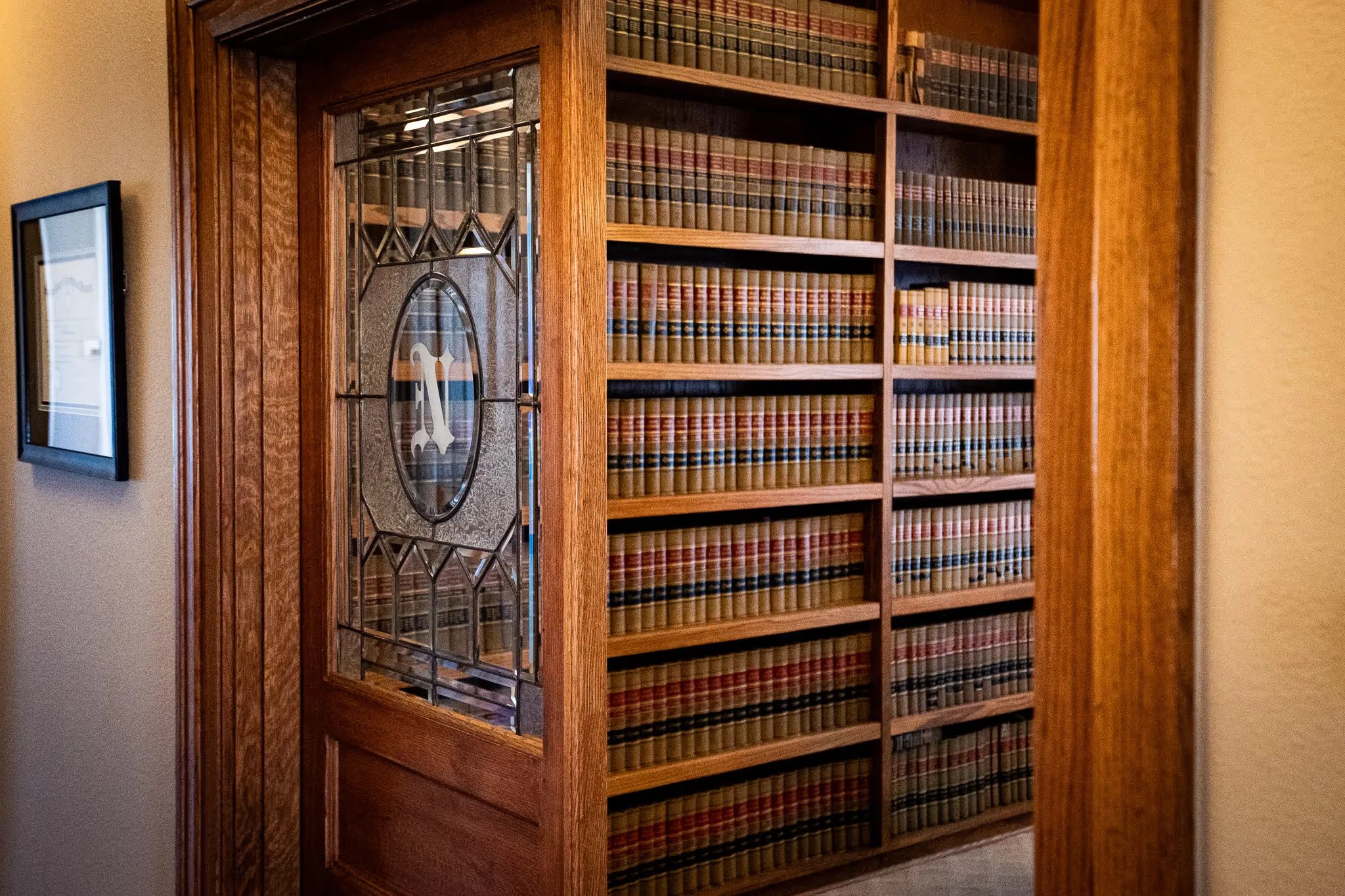 Leaded-glass door with an etched N monogram opening onto shelves of law reporters at Nelson Law Firm.