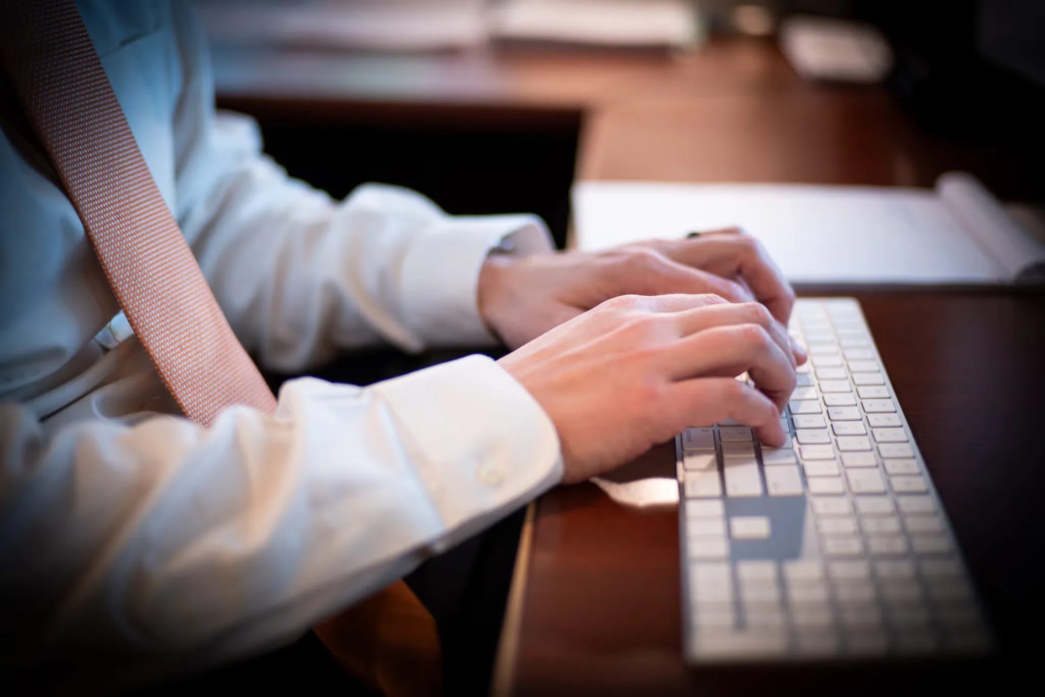 Close-up of hands on a white keyboard at a dark wood desk at Nelson Law Firm, shirt cuffs and tie in frame.