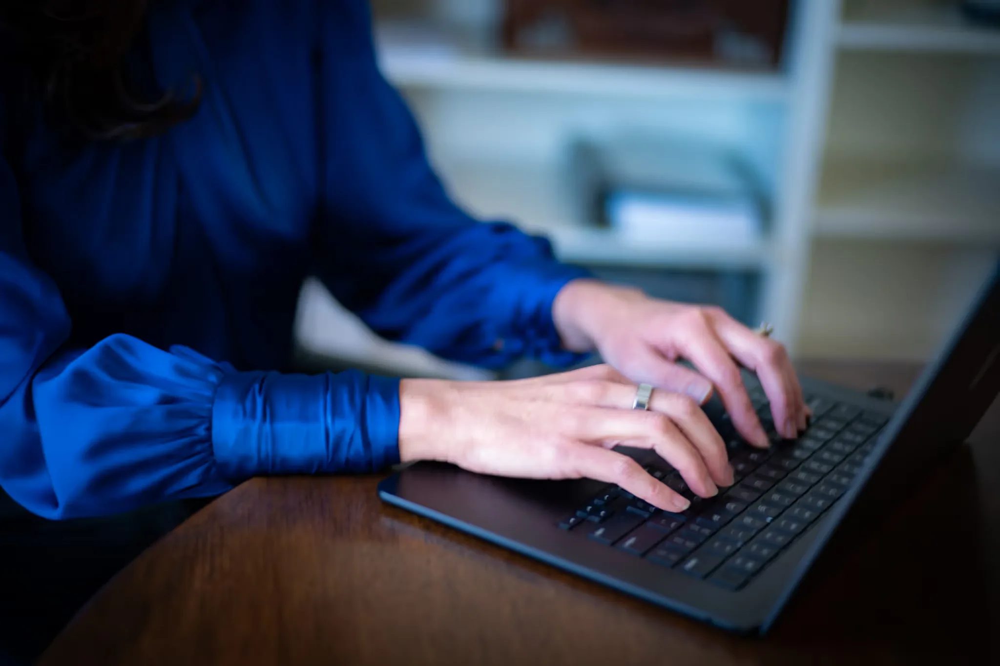 Close-up of hands typing on a laptop keyboard in blue satin sleeves at a wood table in the Nelson Law Firm library.