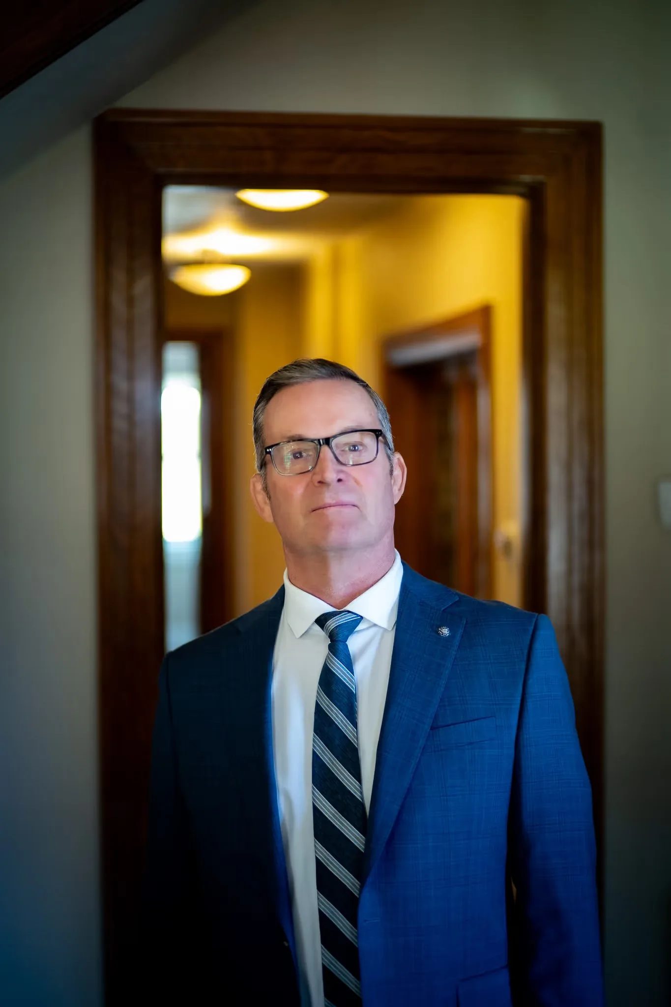 Mark W. Nelson, founder of Nelson Law Firm, wearing glasses in a doorway of the firm's Denver office with a lamplit hallway behind