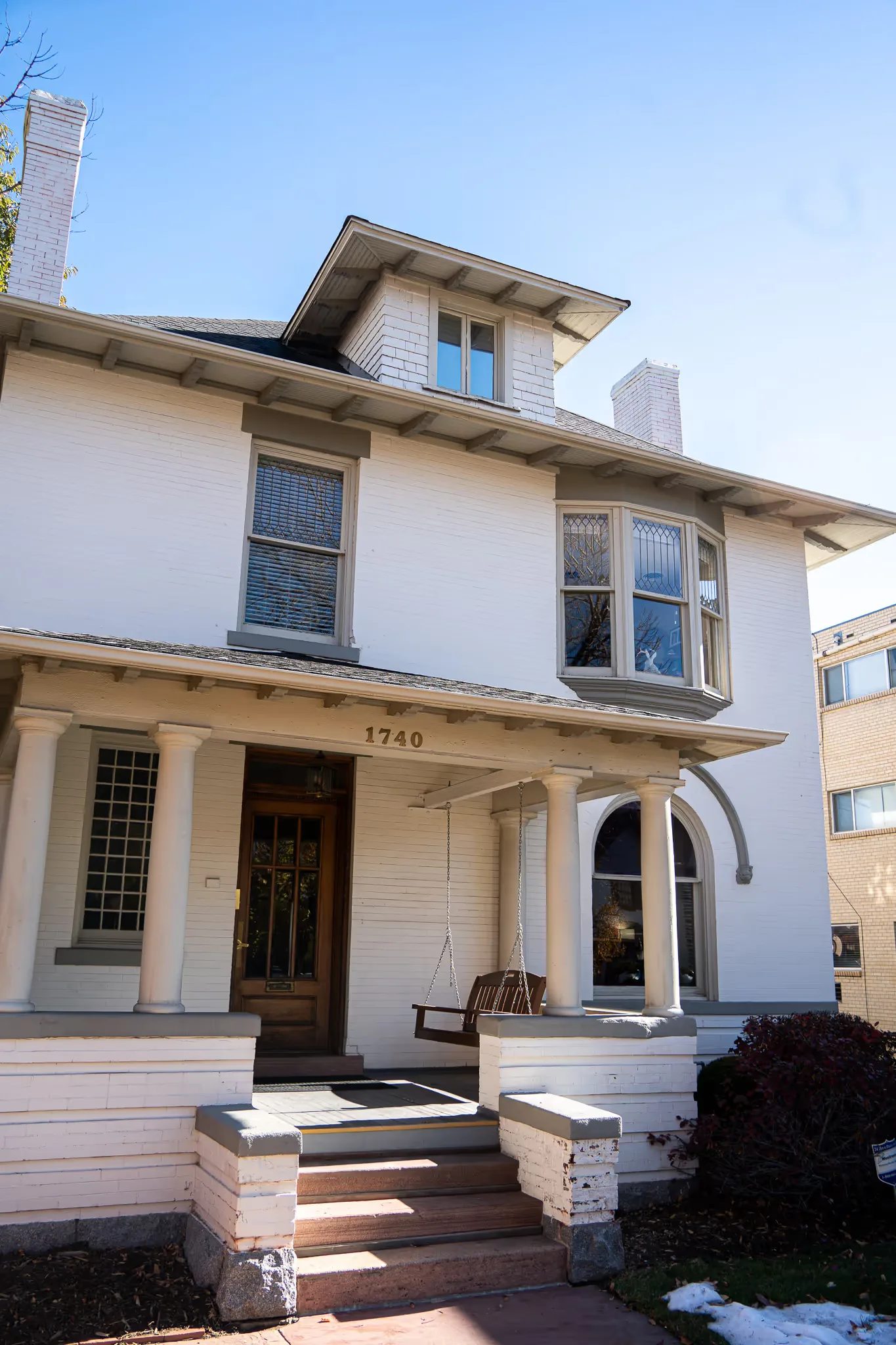 Two-storey white brick house with dormer, bay window and columned porch, the Nelson Law Firm office at 1740 N High Street in Denver