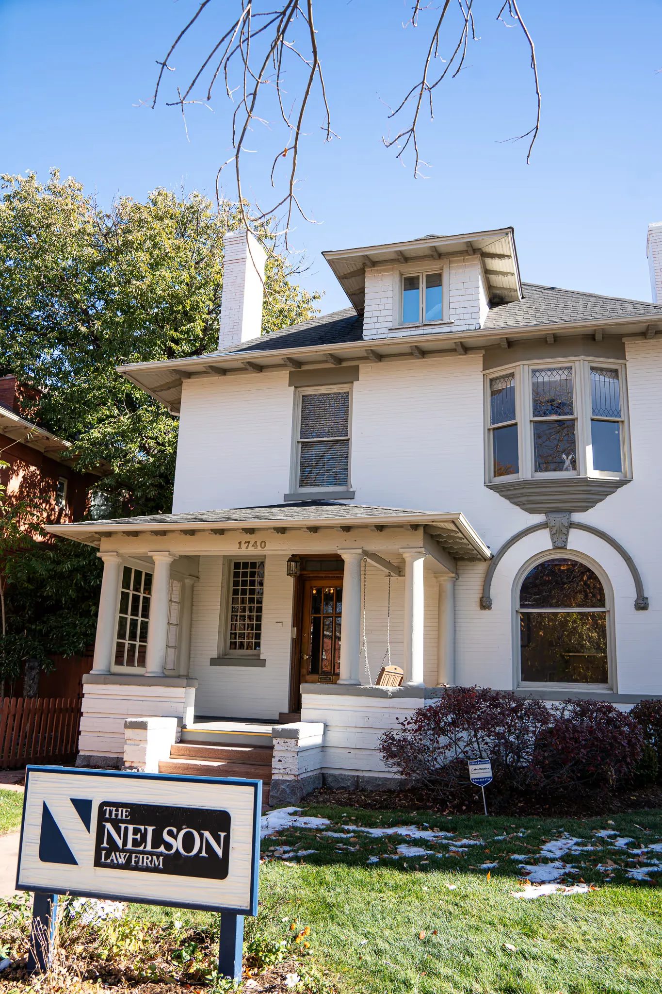 The Nelson Law Firm sign on the lawn in front of the firm's historic white brick house in Denver under a blue sky