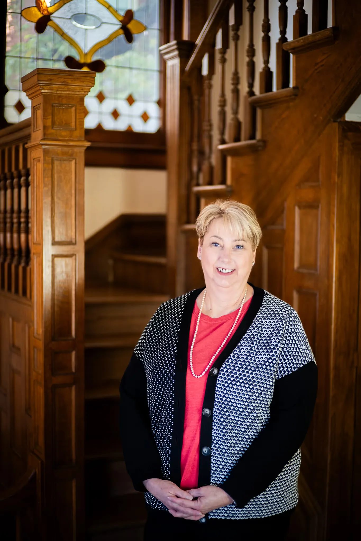 A Nelson Law Firm staff member in a red top and patterned cardigan with hands clasped at the oak staircase in Denver