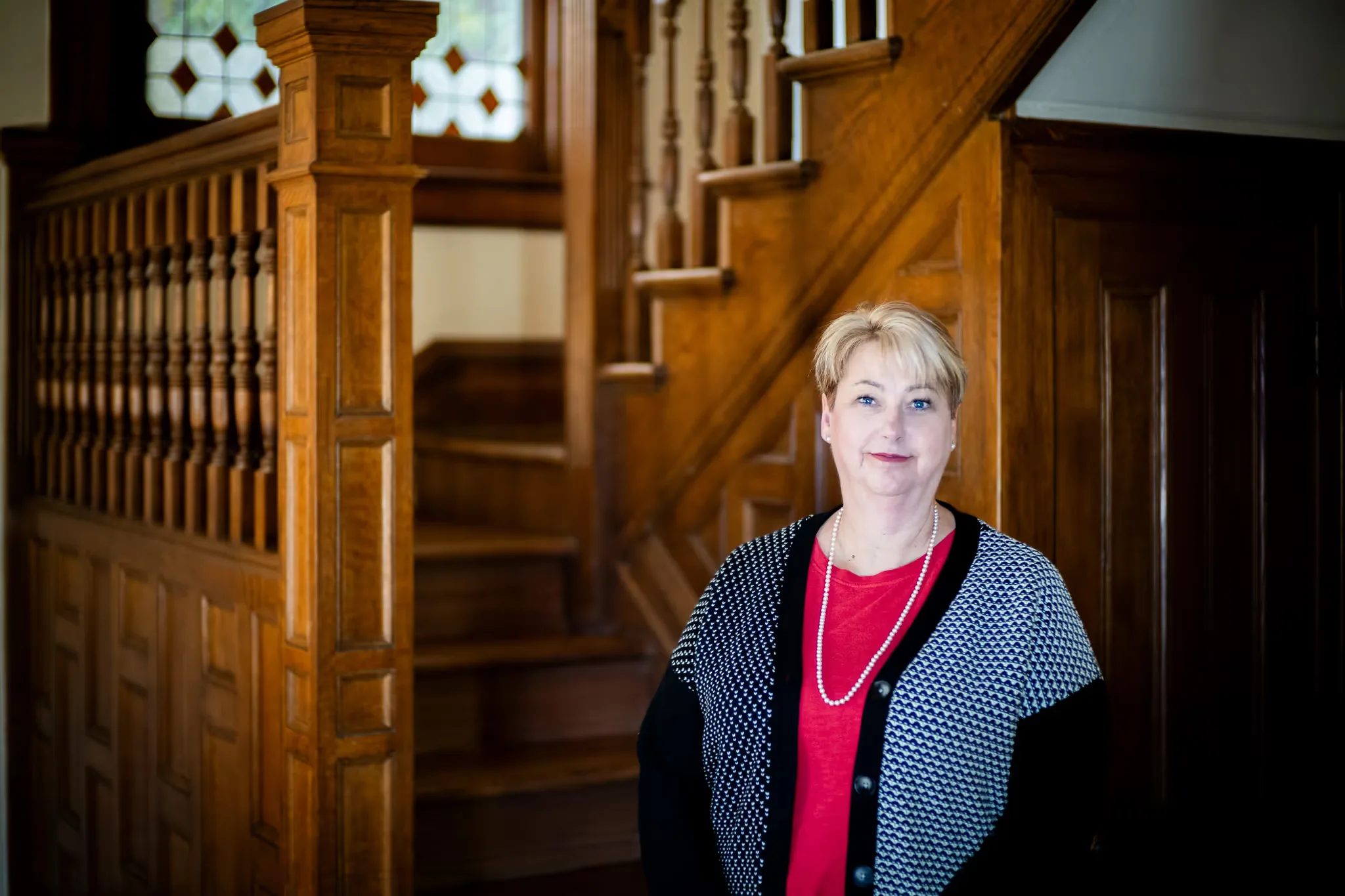 A Nelson Law Firm staff member wearing a pearl necklace and patterned cardigan beside the staircase newel post in Denver