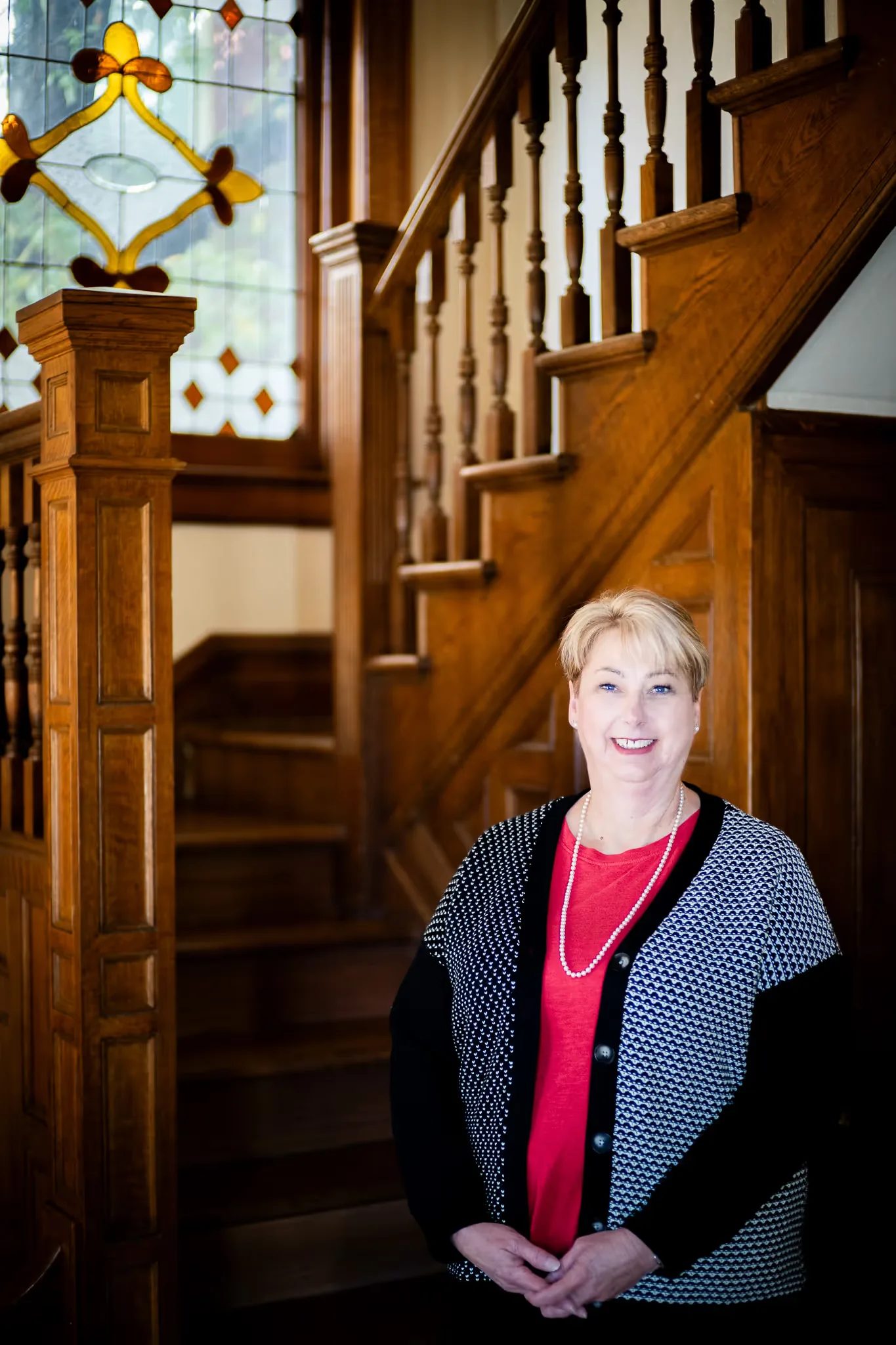 A Nelson Law Firm staff member in a red top smiling broadly at the oak staircase of the firm's Denver office