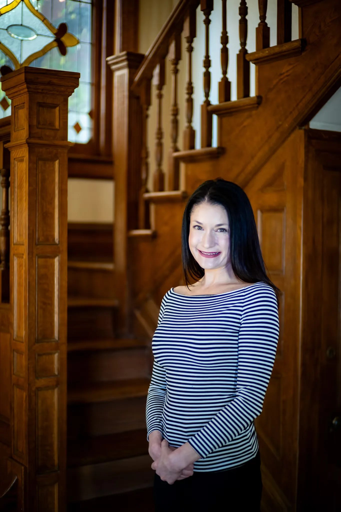 A Nelson Law Firm staff member in a striped top standing with hands clasped beside the oak staircase in the firm's Denver office