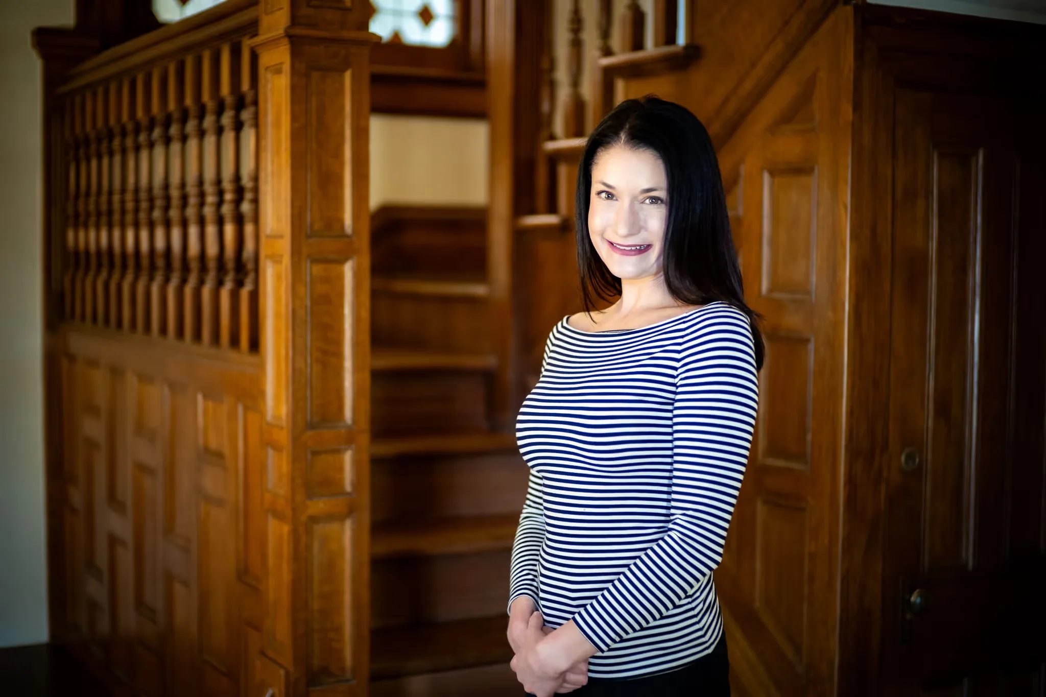 A Nelson Law Firm staff member in a striped top smiling in front of the oak staircase of the firm's Denver office