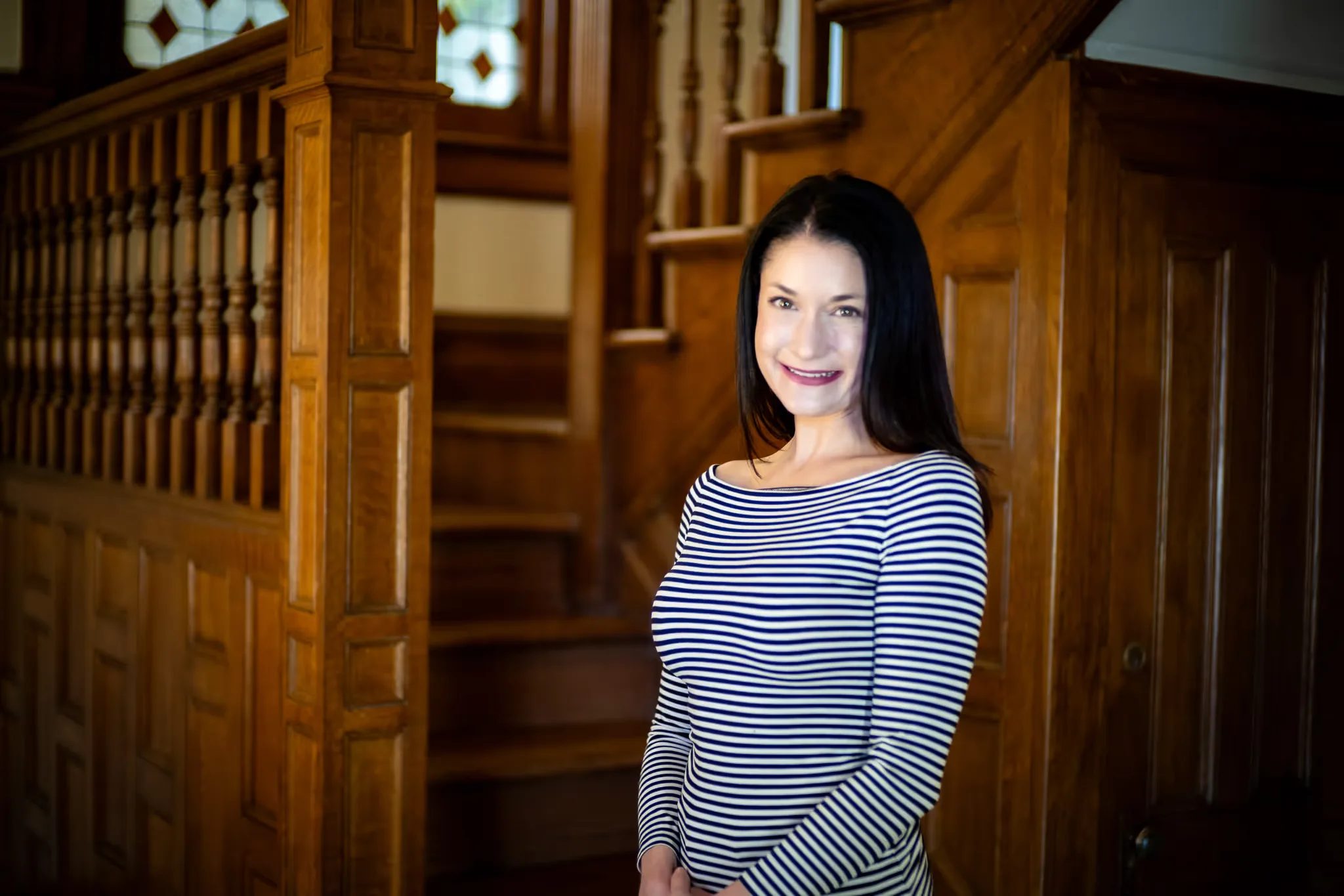 A Nelson Law Firm staff member in a striped top with hands clasped in front of the oak staircase in Denver